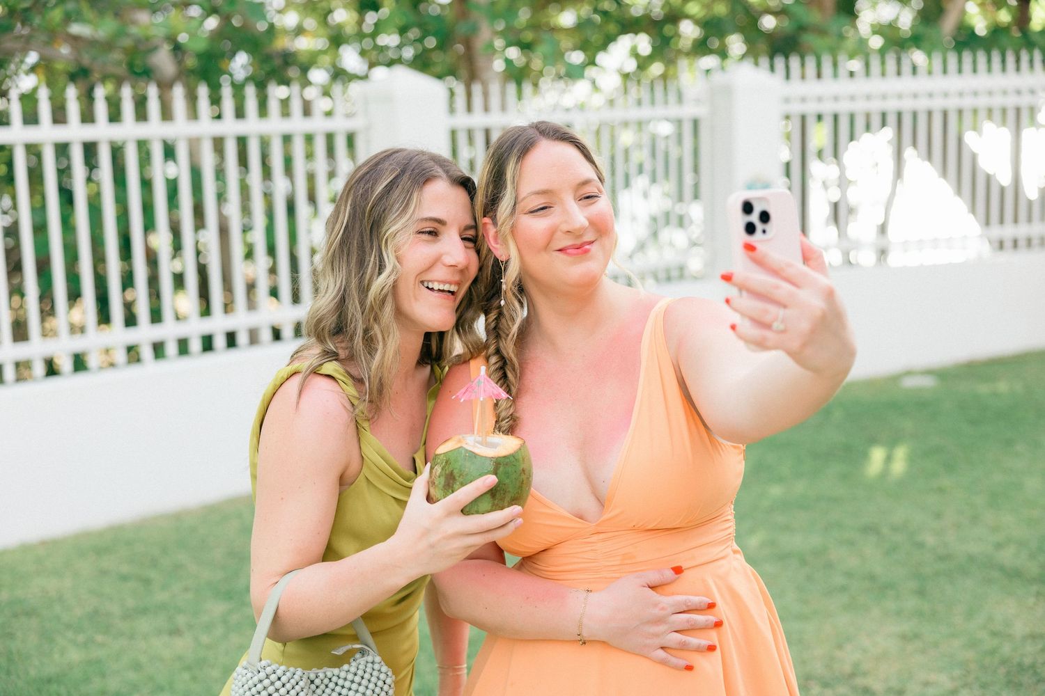Two friends in summer dresses taking a selfie while holding coconut drinks.