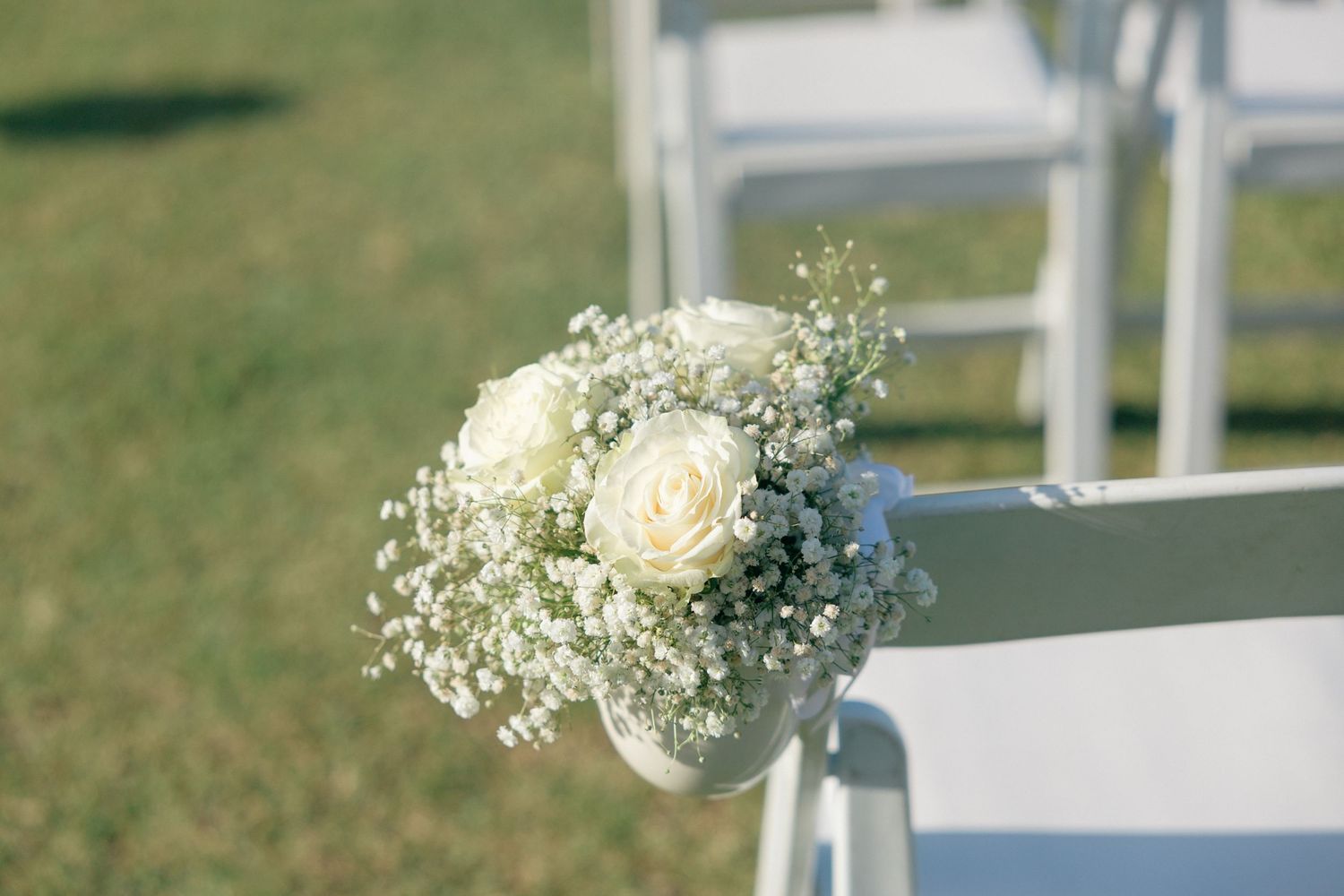 White roses and baby's breath floral arrangement decorating a ceremony chair.