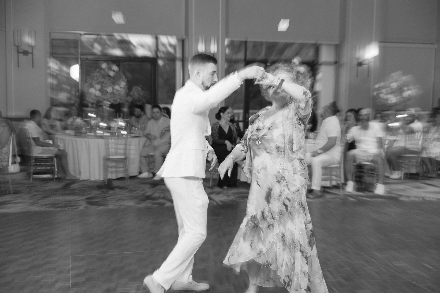 Wedding guests dance together on a patterned floor during an indoor reception.