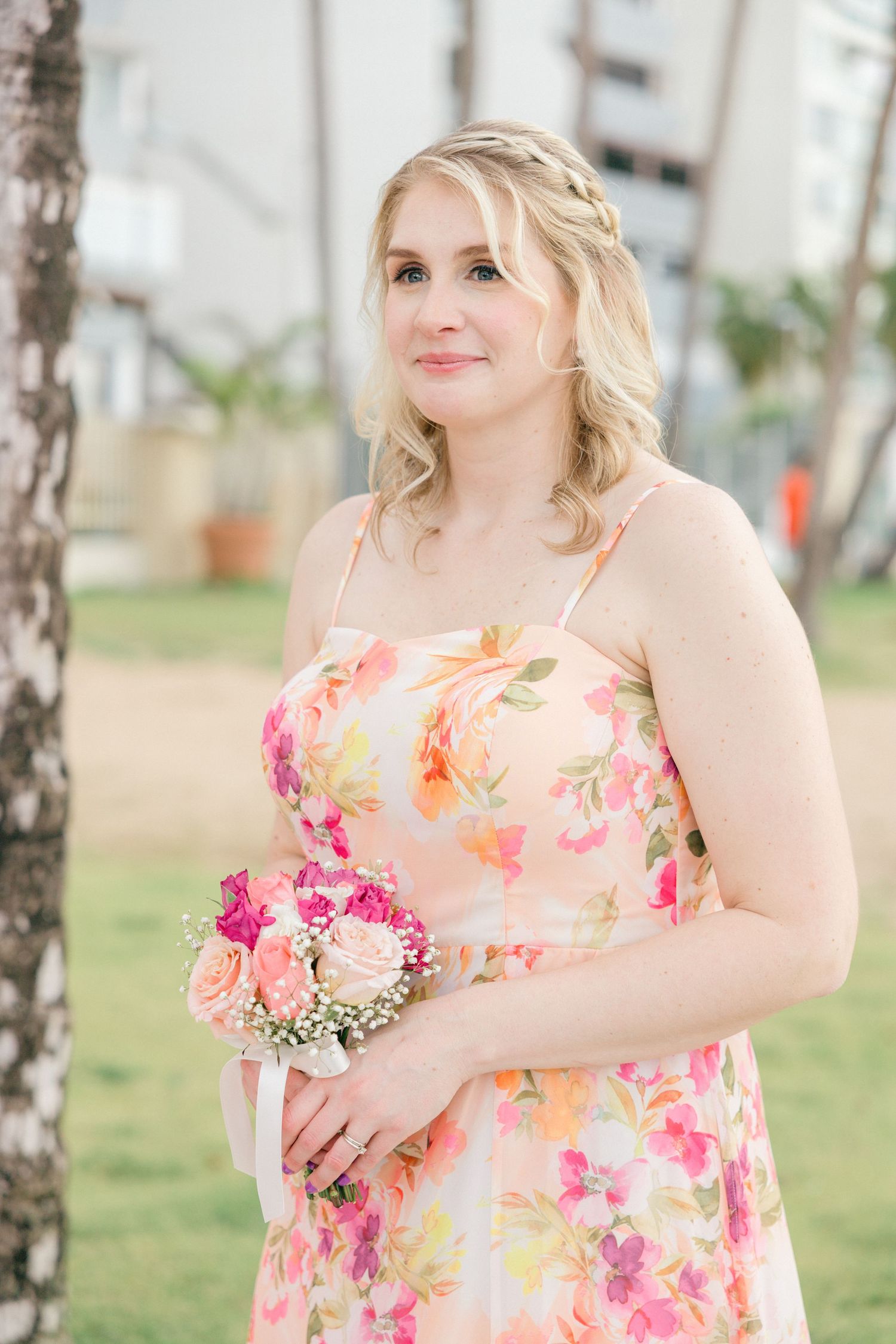 Bridesmaid in floral print dress holds pink bouquet during outdoor ceremony.