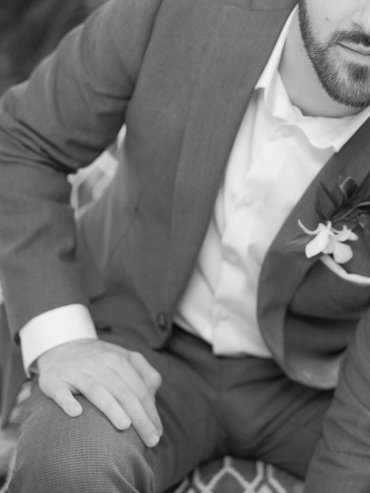 Groom in gray suit with boutonniere sitting in formal pose.