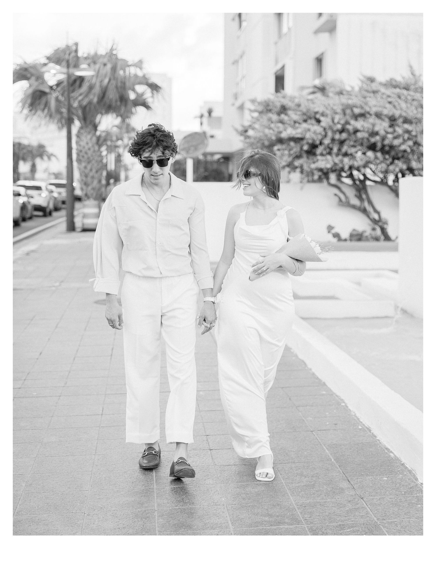 Couple walking together on a tiled pathway wearing matching white outfits.
