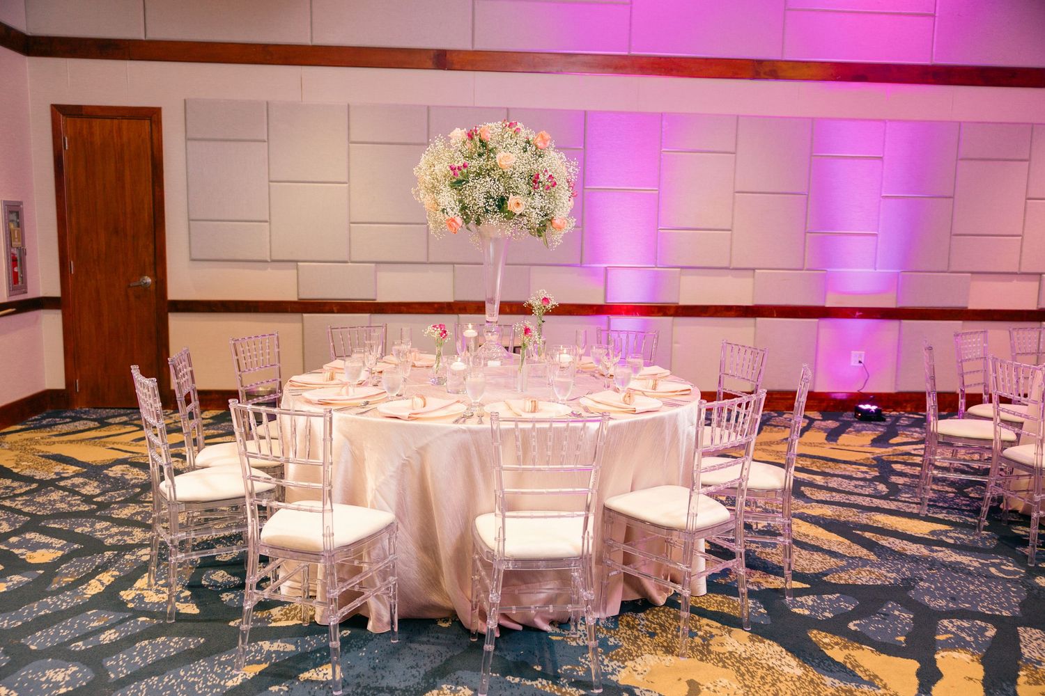 Wedding reception venue with round tables and pink ambient lighting.