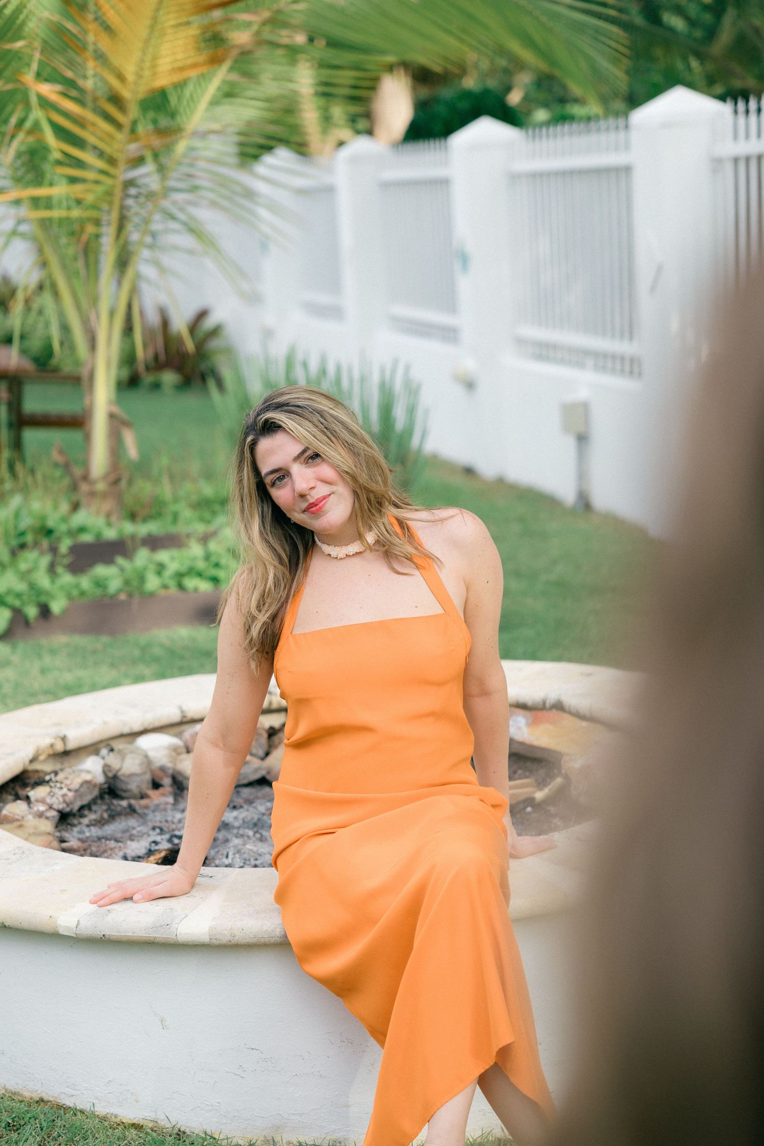 Woman in bright orange dress posing in tropical garden setting.
