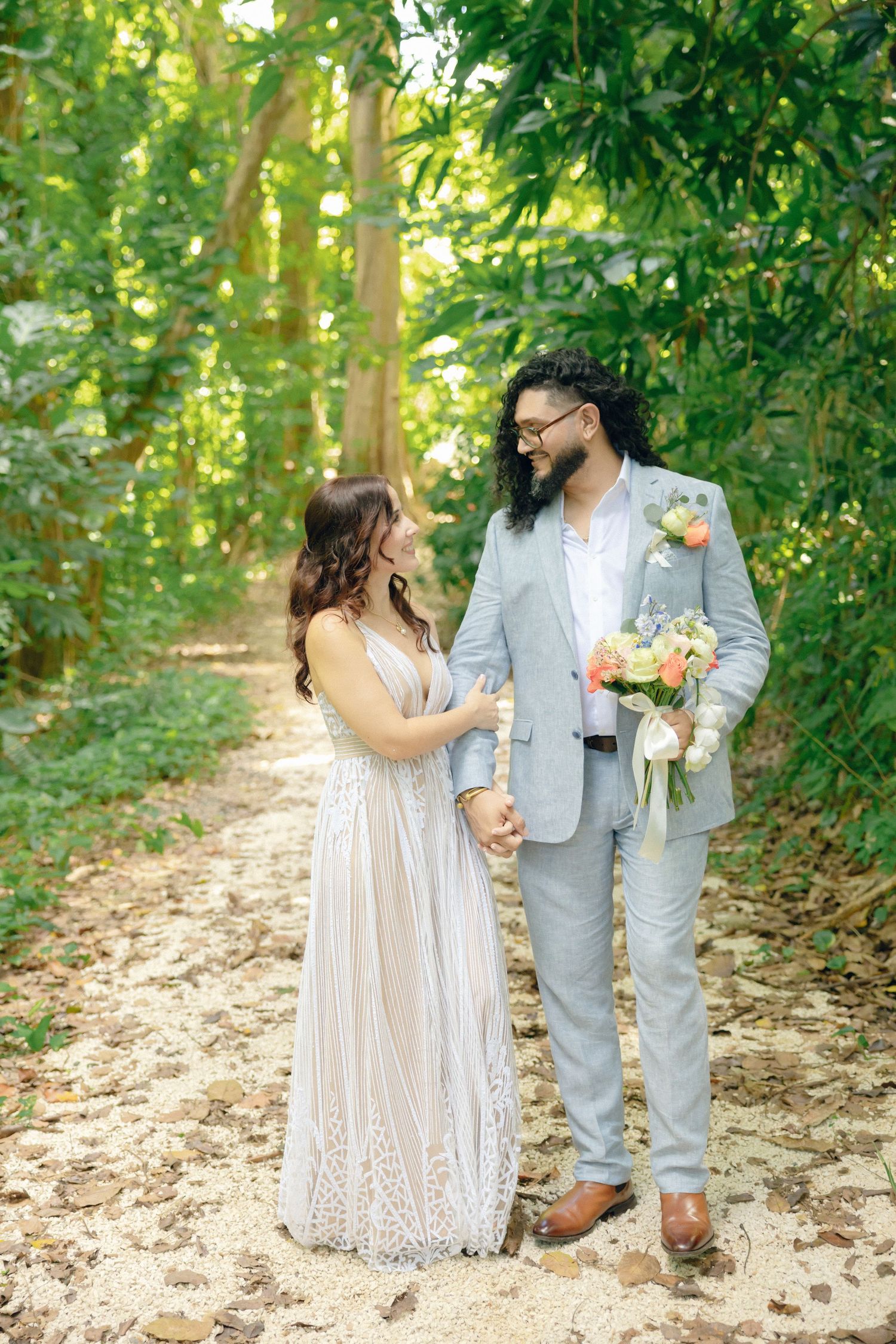 Romantic couple in wedding attire walking along a tree-lined path on their special day.