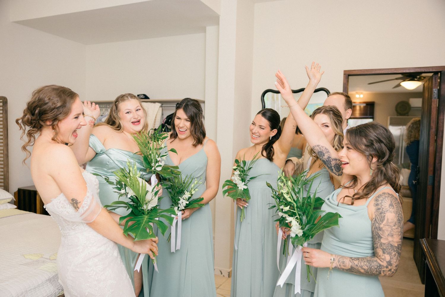 Wedding party in sage green dresses sharing joyful candid moments during pre-ceremony preparations.