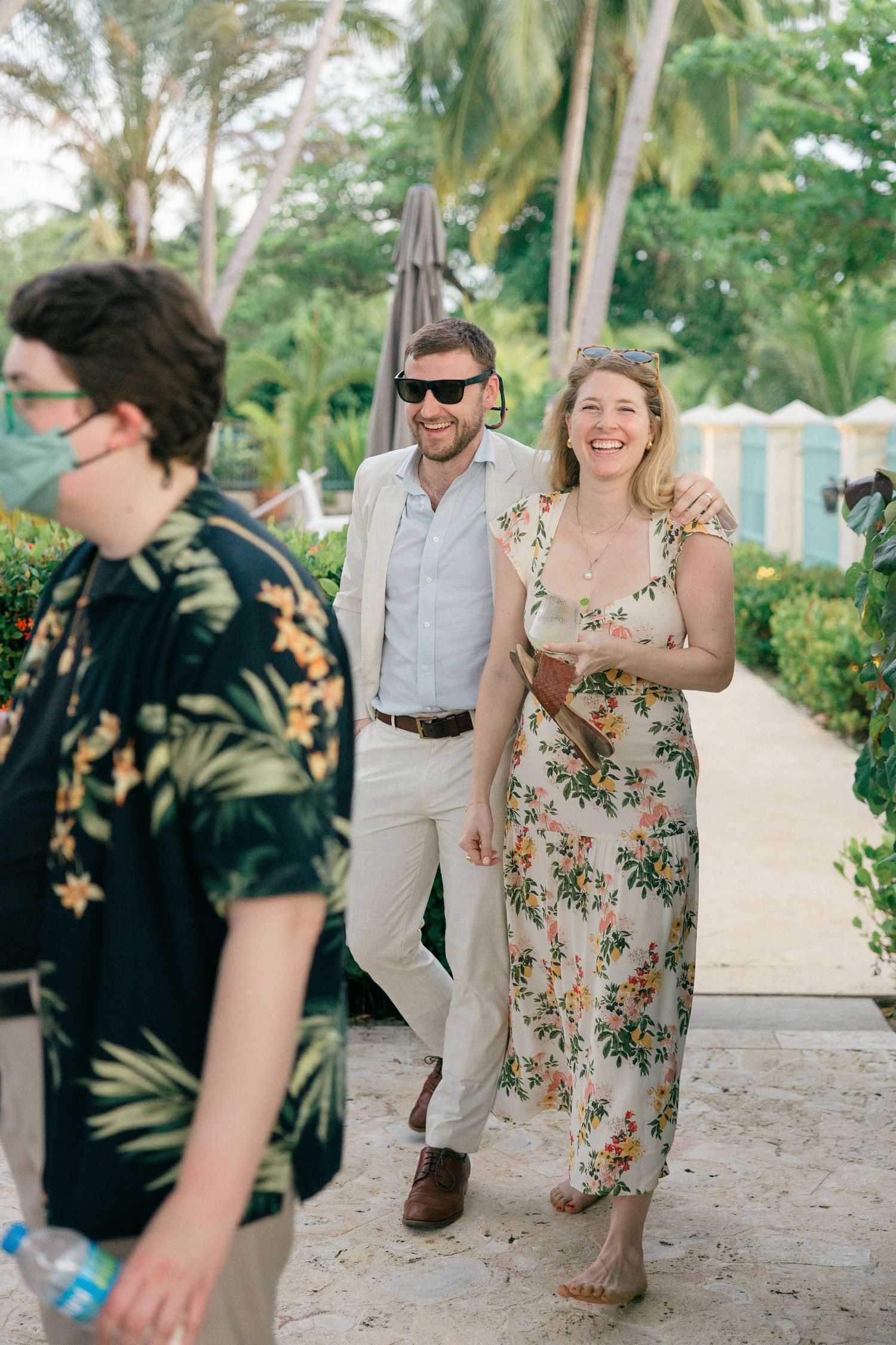 Wedding guests in tropical attire dance and celebrate on a sandy beach with palm trees in the background.