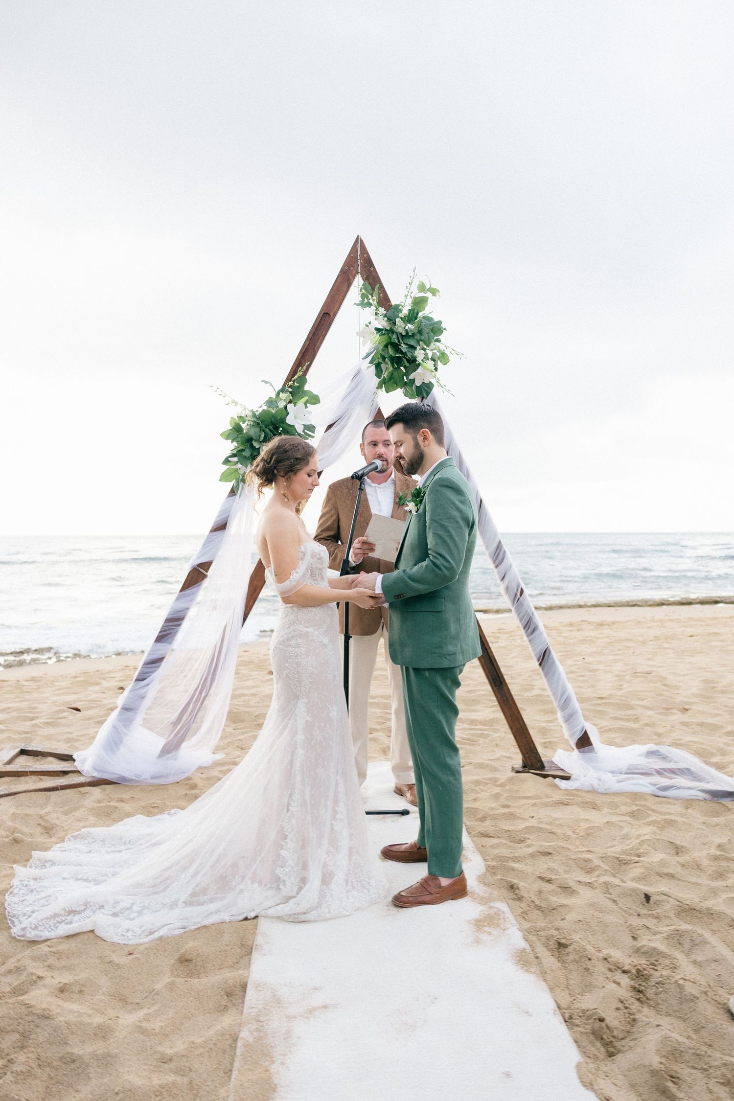 Couple shares romantic moments under a triangular arch on a sandy beach.