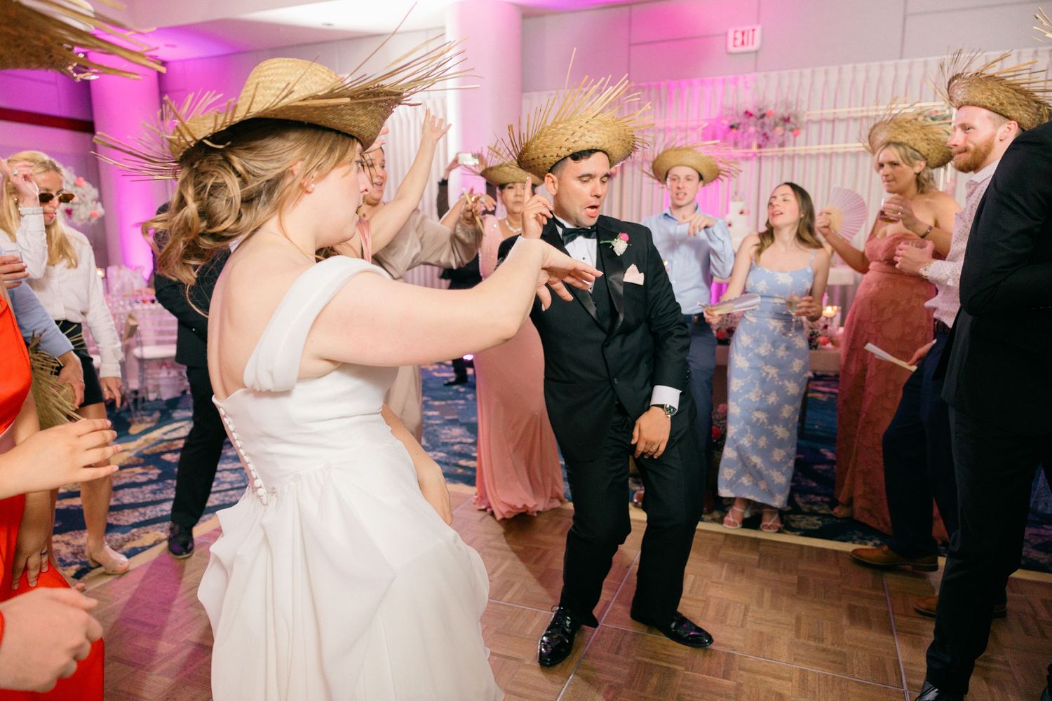 Wedding reception dance floor scene with pink uplighting and guests in formal attire.