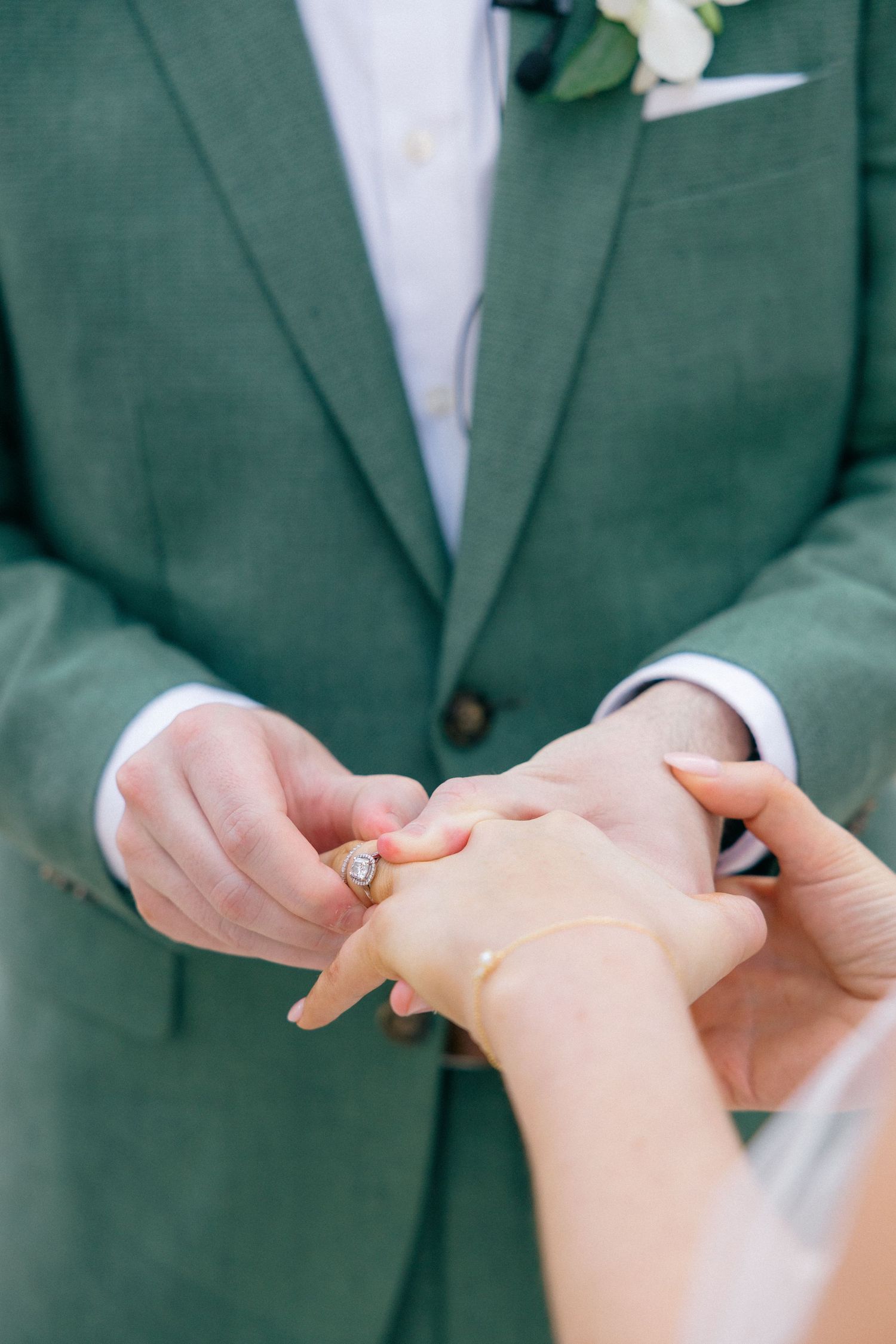 Close-up of hands exchanging rings during wedding ceremony with green suit visible.