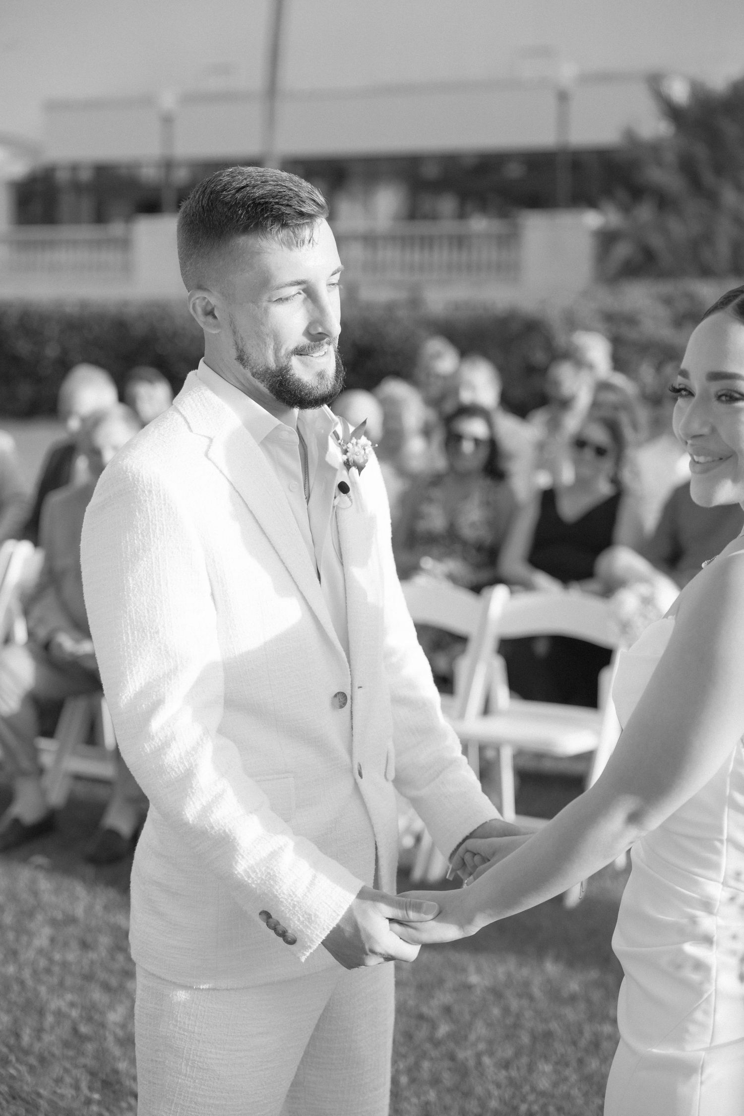 Wedding ceremony participants in white attire exchanging greetings outdoors.