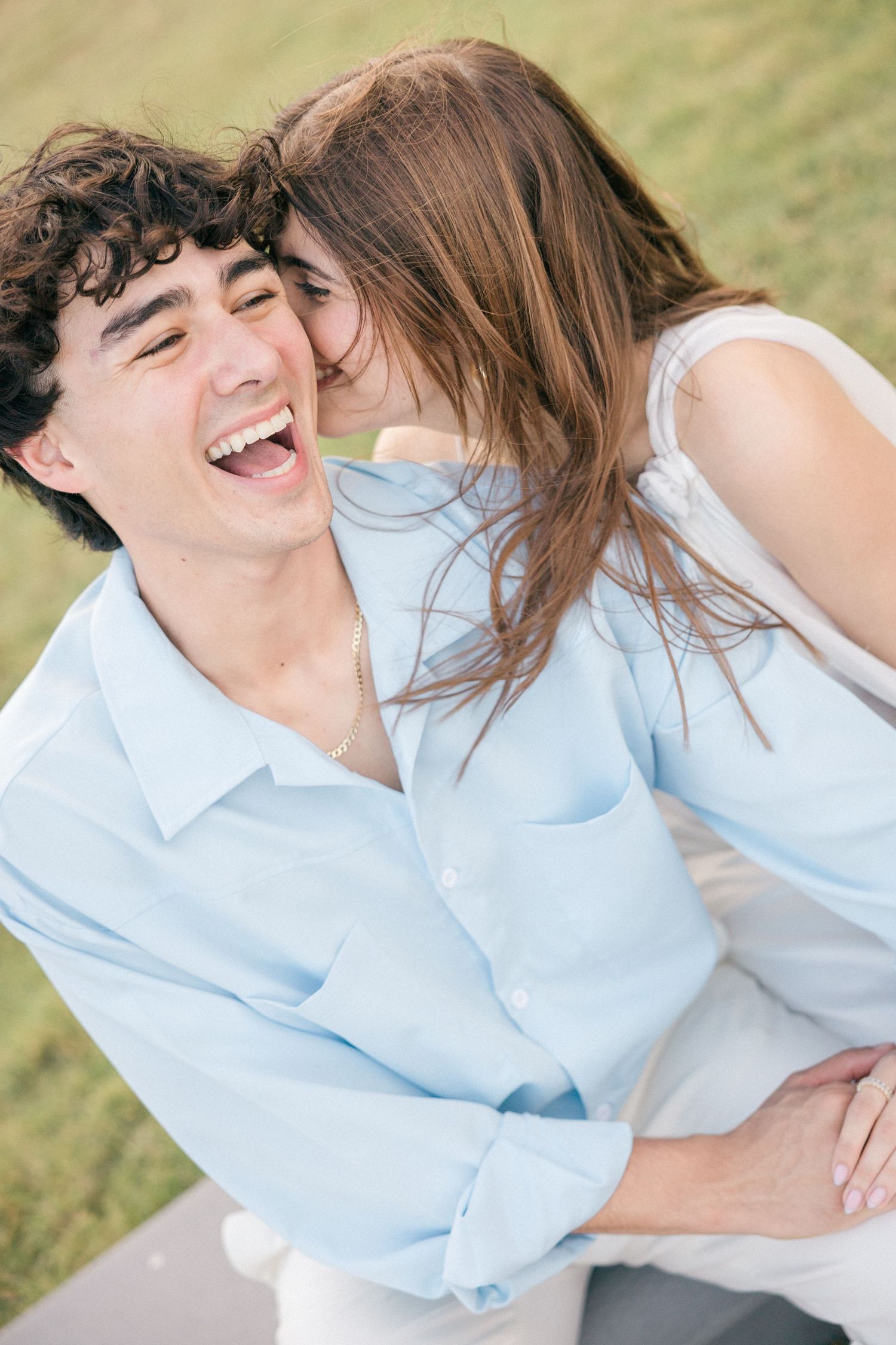 Joyful couple laughing and embracing outdoors in casual blue and white attire.