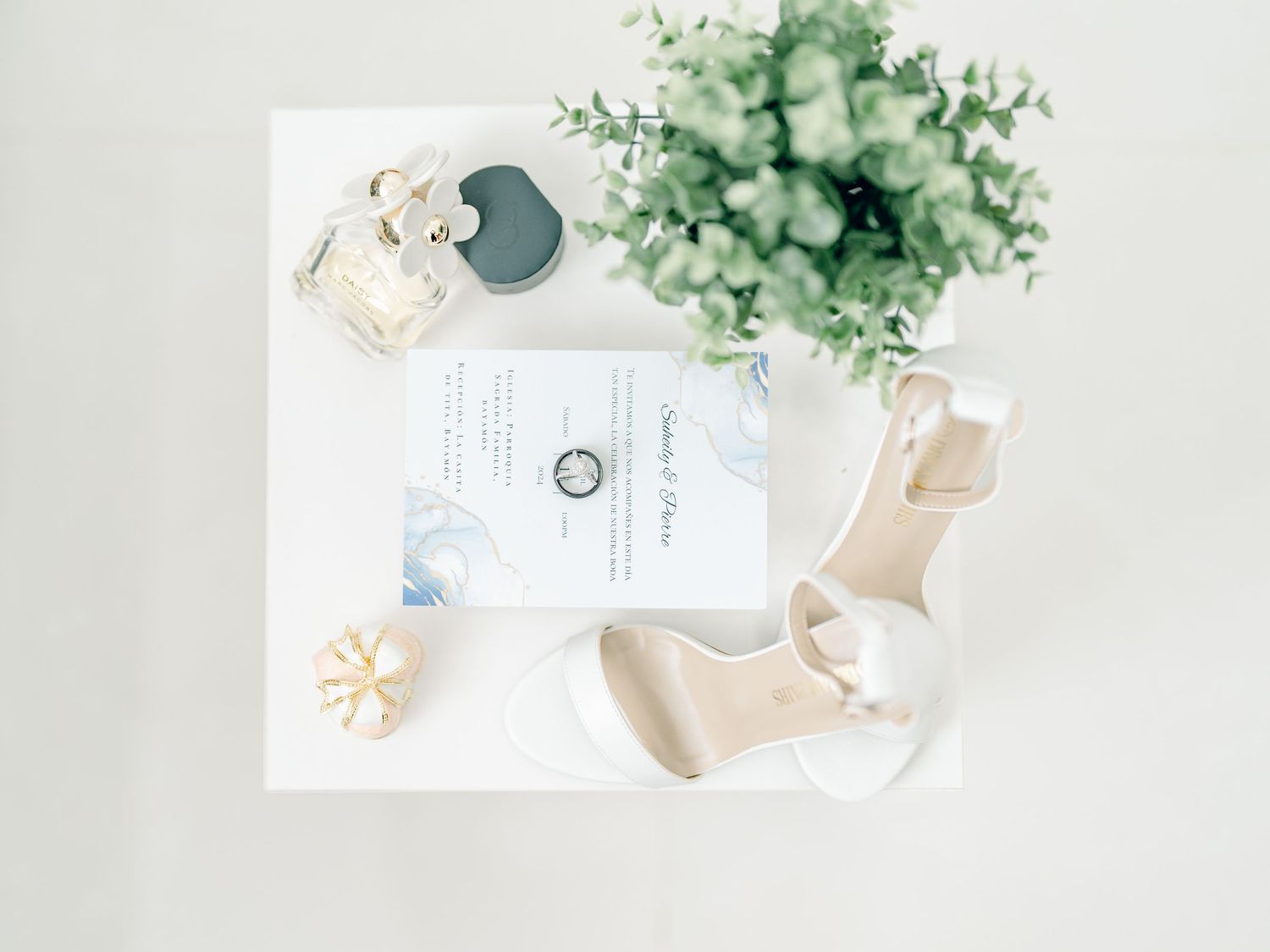 Wedding stationery flatlay with eucalyptus leaves and white floral arrangements on light background.