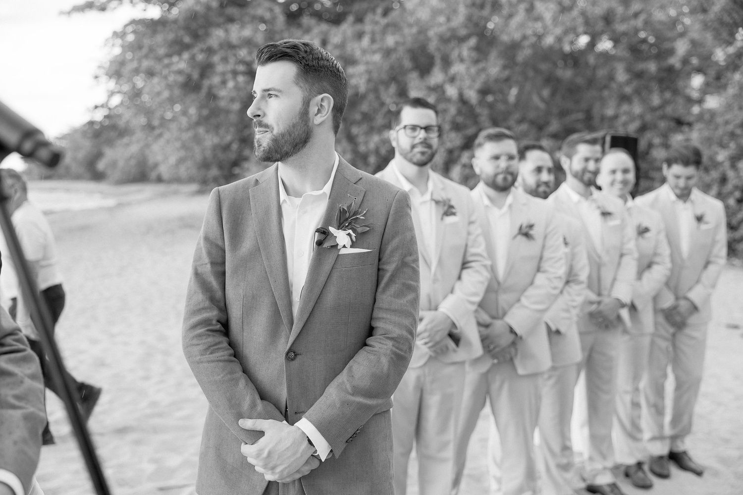 Wedding party members in formal attire gather on a beach for ceremony photos.