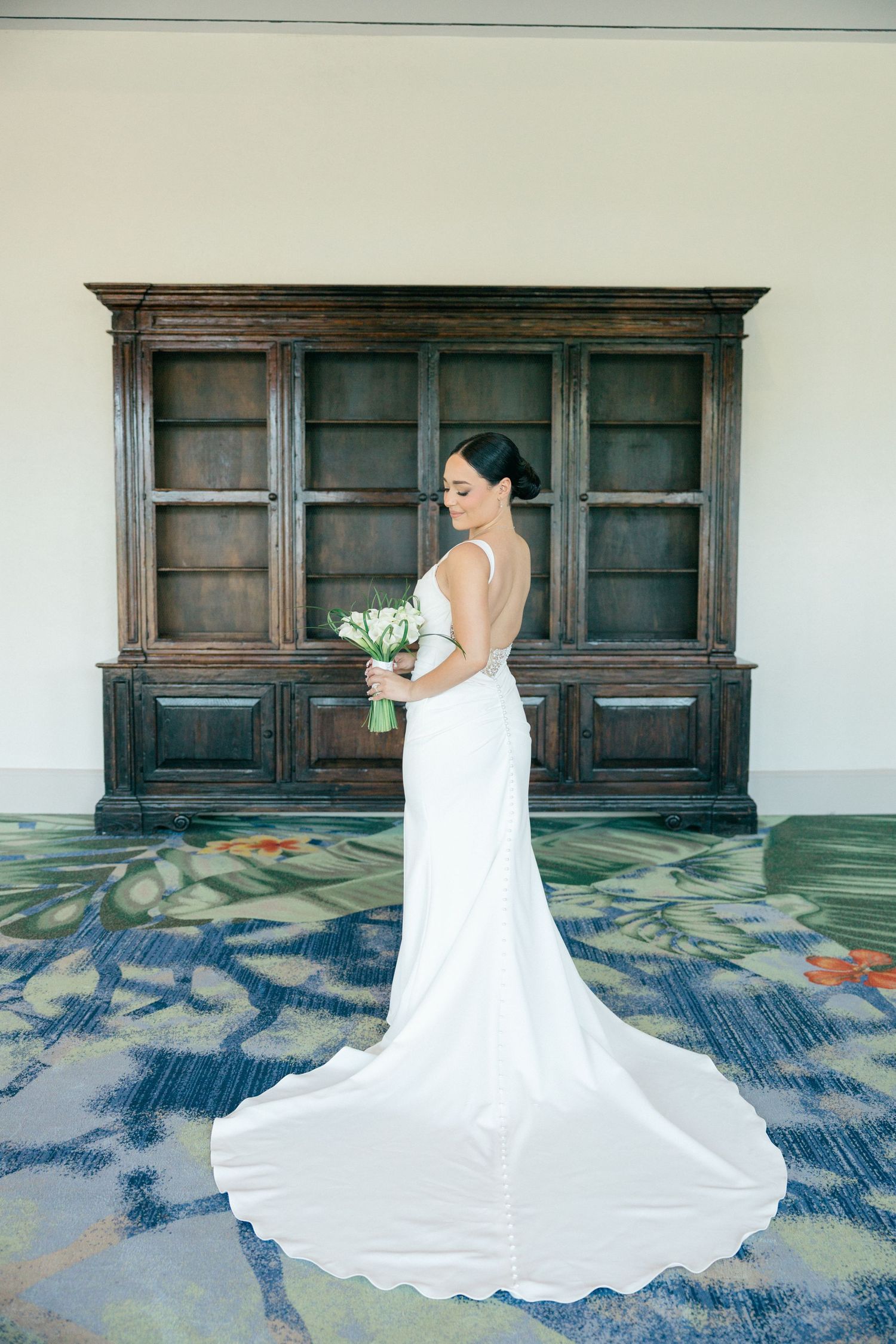 Bride in flowing white gown poses against dark wood panels on blue patterned floor.