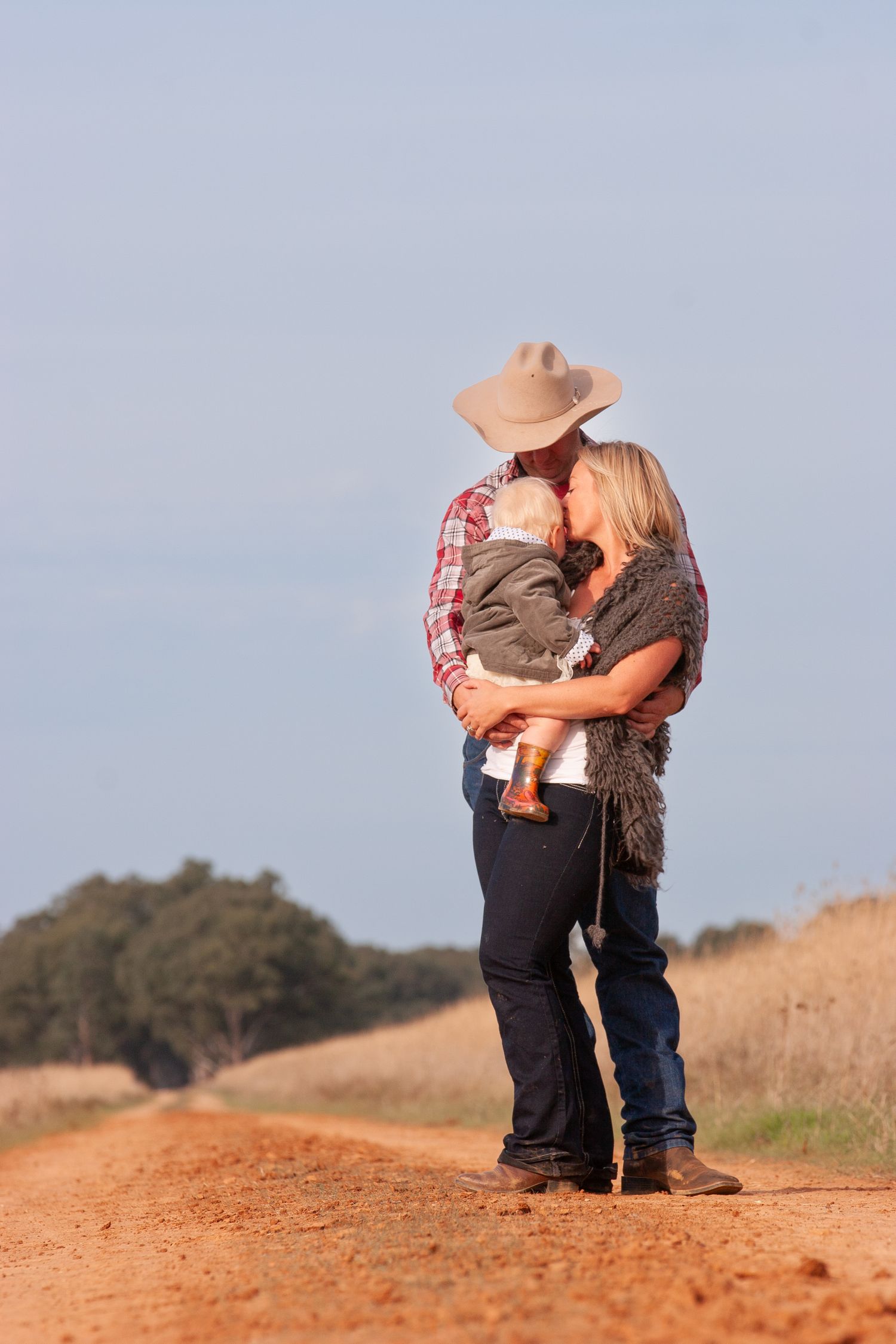 A couple embraces on a rustic dirt road in the countryside during golden hour.