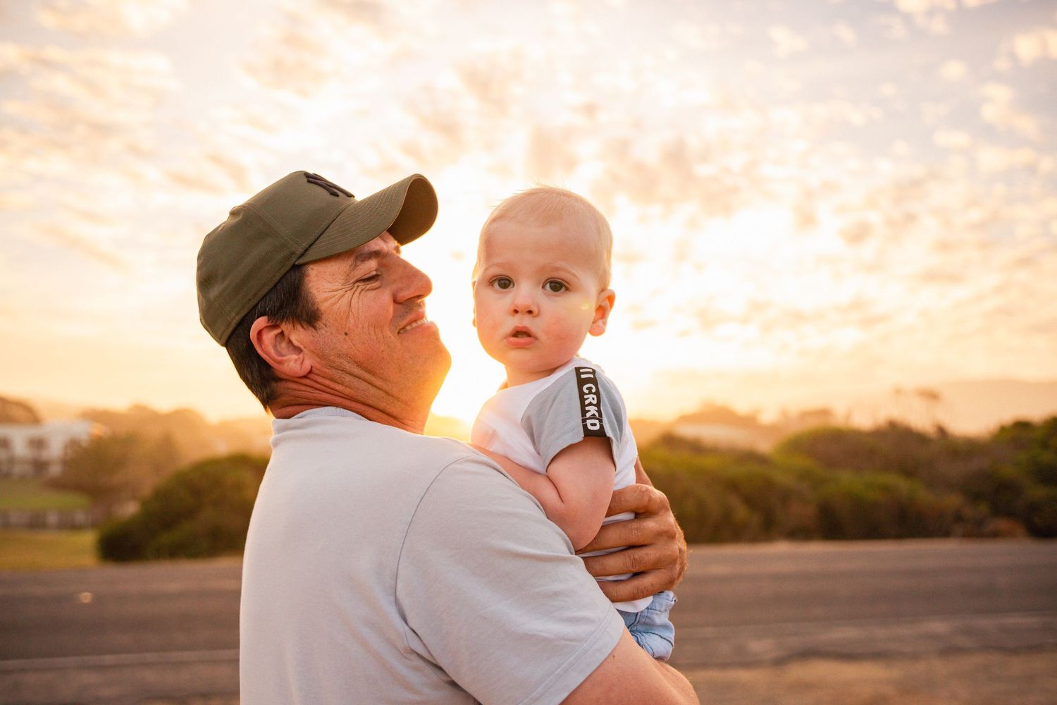 Parent holds baby against beautiful sunset sky in an outdoor setting.