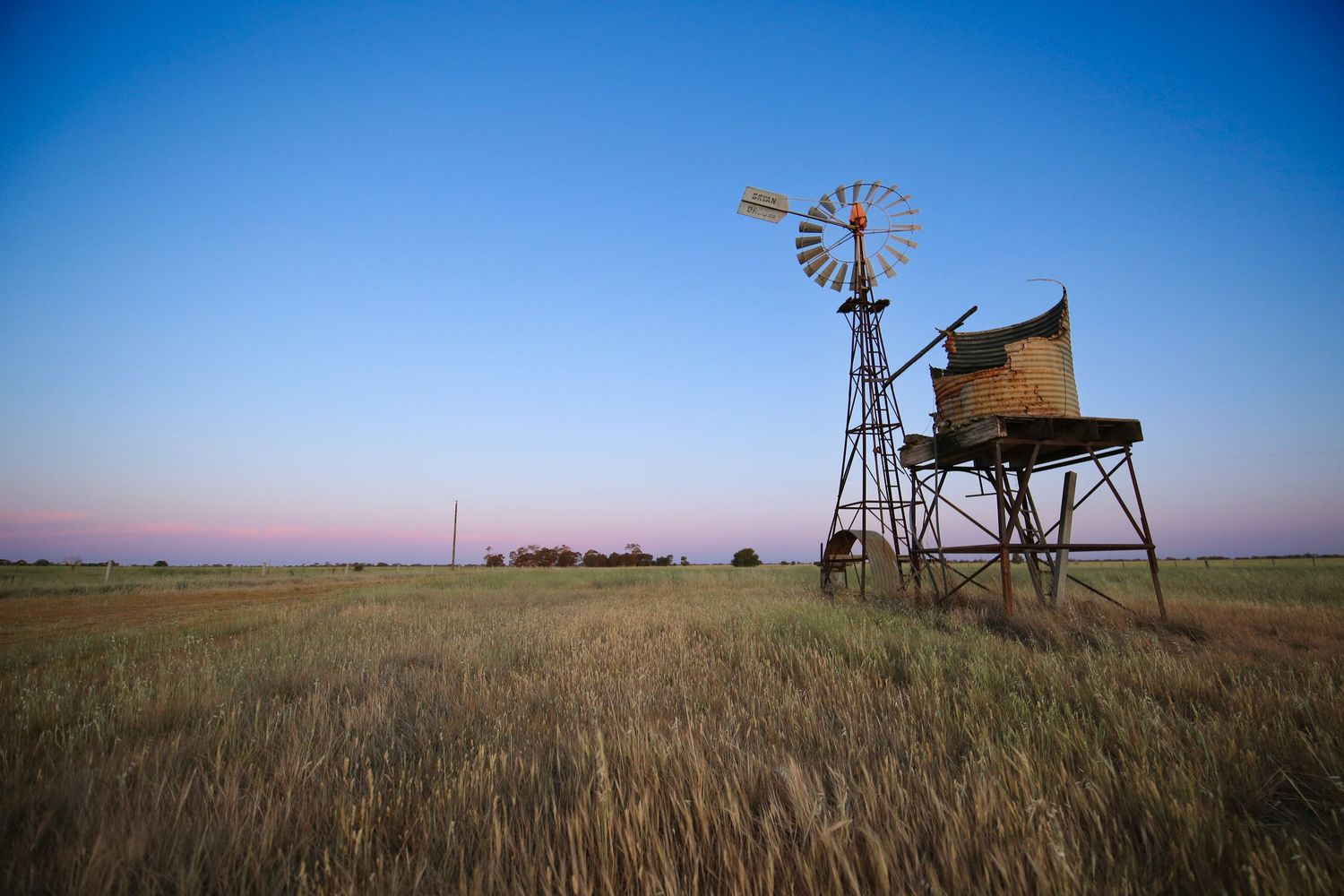 A vintage windmill and water tank stand in a grassy field against a clear blue sky.