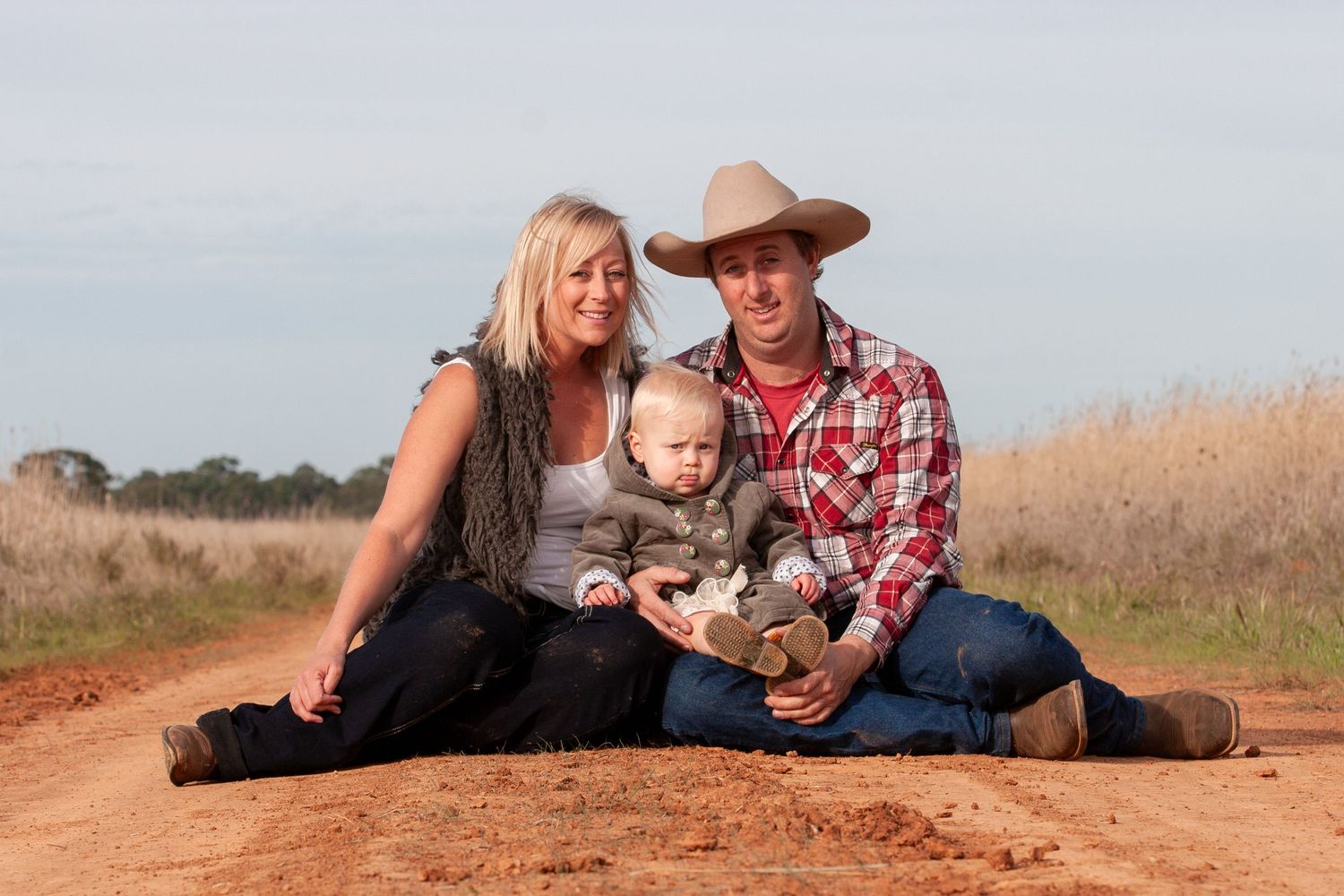 Family sits together on rustic dirt road for outdoor portrait session.