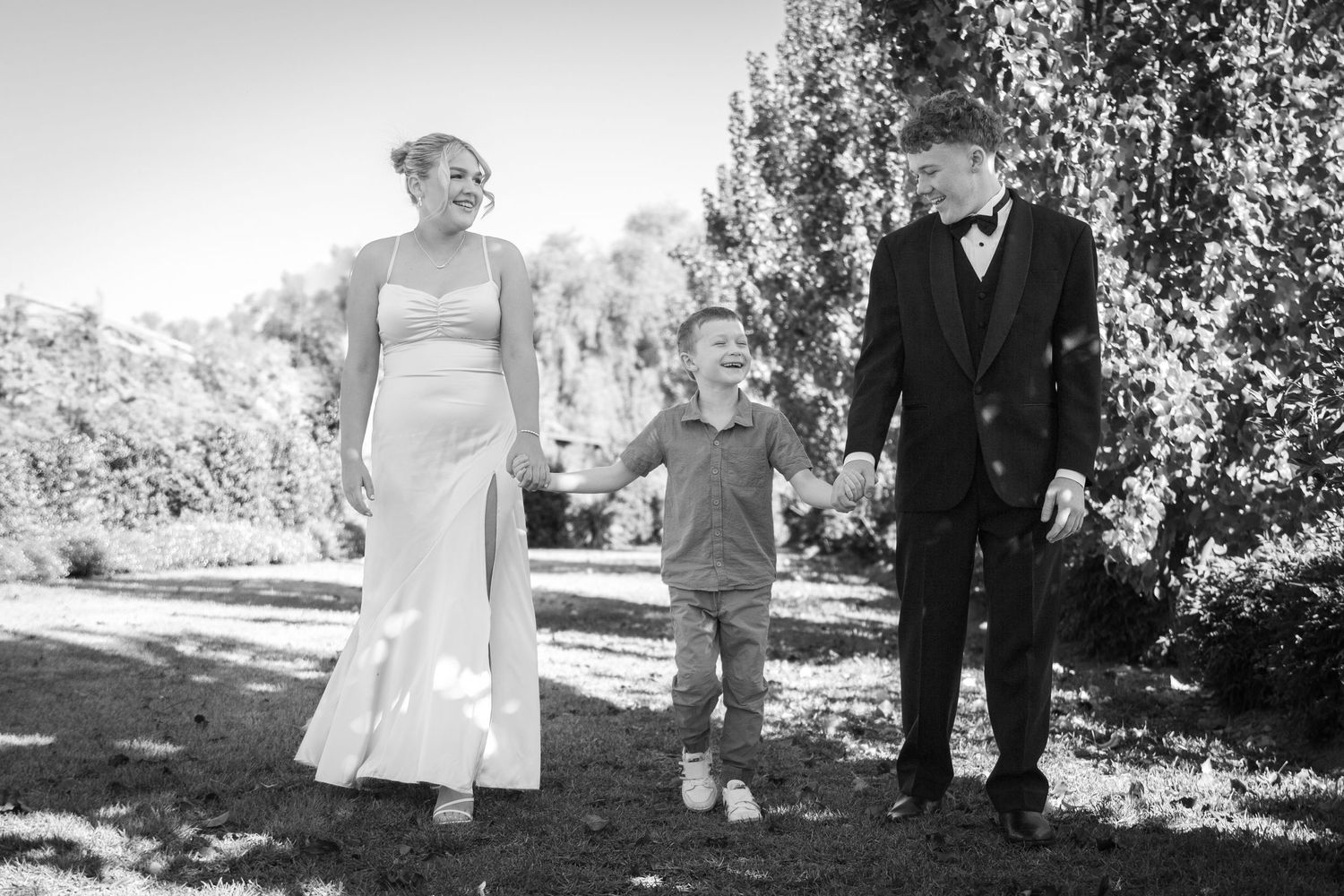 People hold hands while walking together in a garden path with trees, captured in black and white photography.