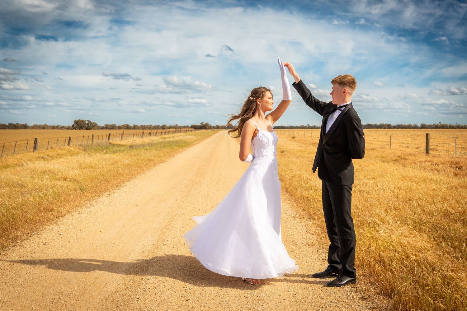 A couple in wedding attire dance together in a golden wheat field at sunset creating a romantic silhouette.