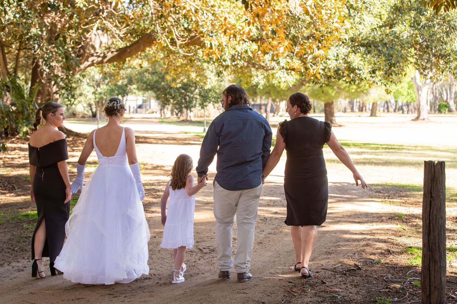 Wedding party walking together down tree-lined path on autumn day.