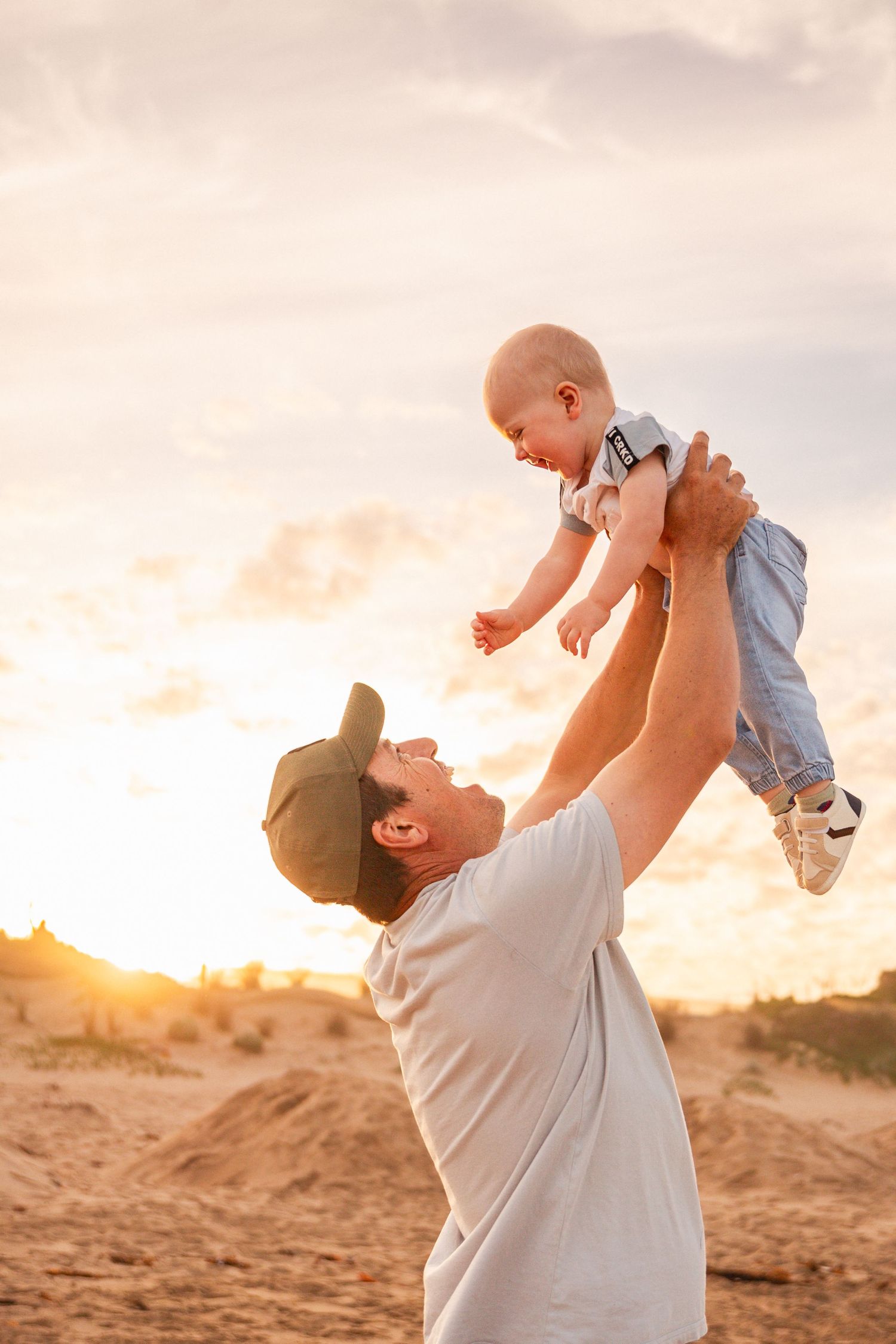 Parent lifts baby high in the air against a golden sunset background.