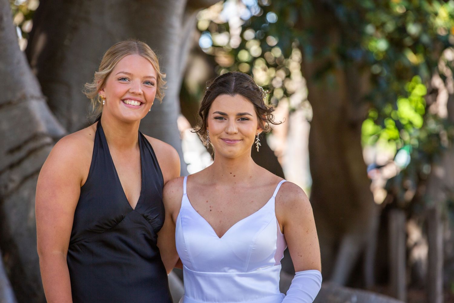 Two bridesmaids in contrasting black and white dresses smiling outdoors.