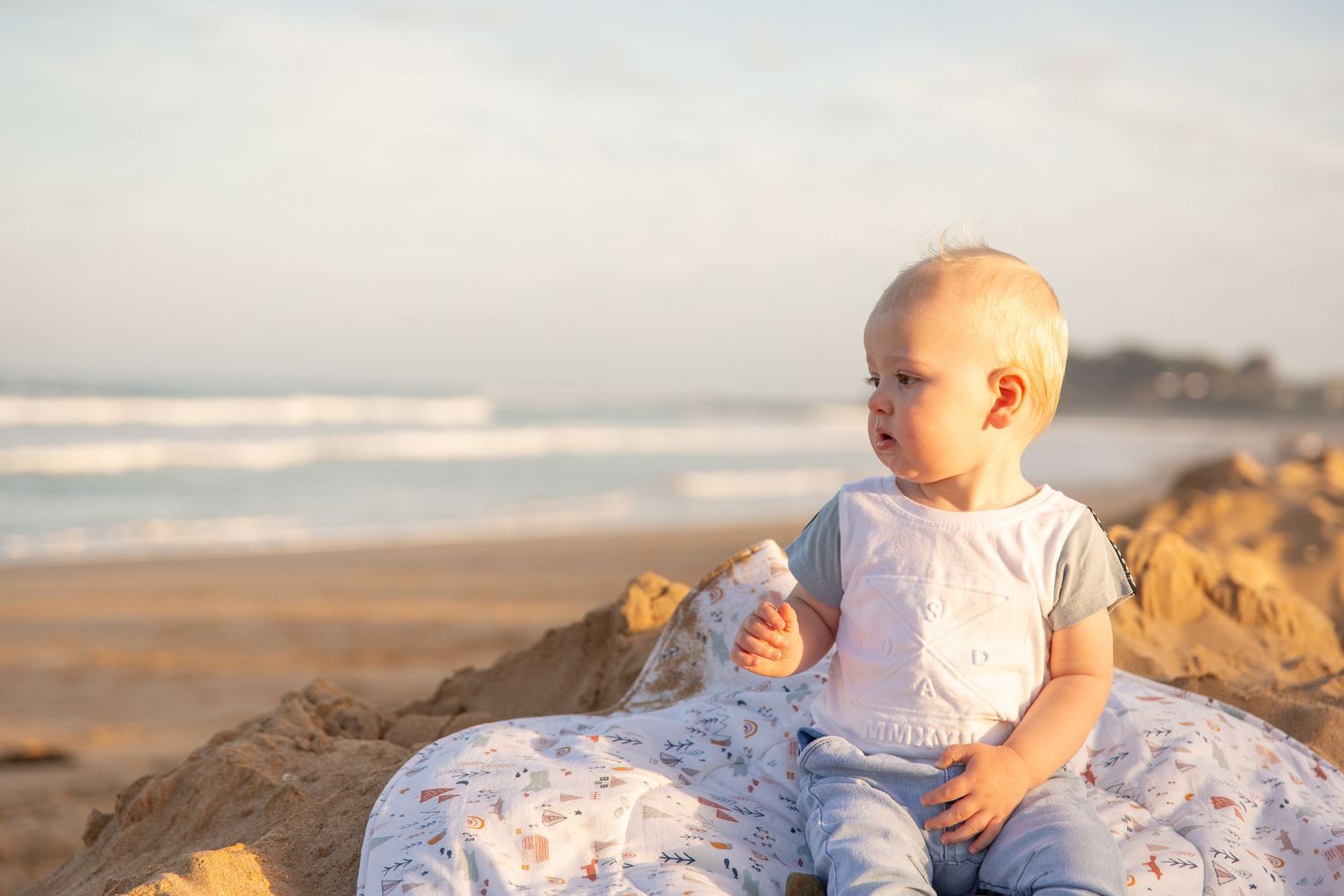 A peaceful beach scene with a little one resting on blankets during sunset.