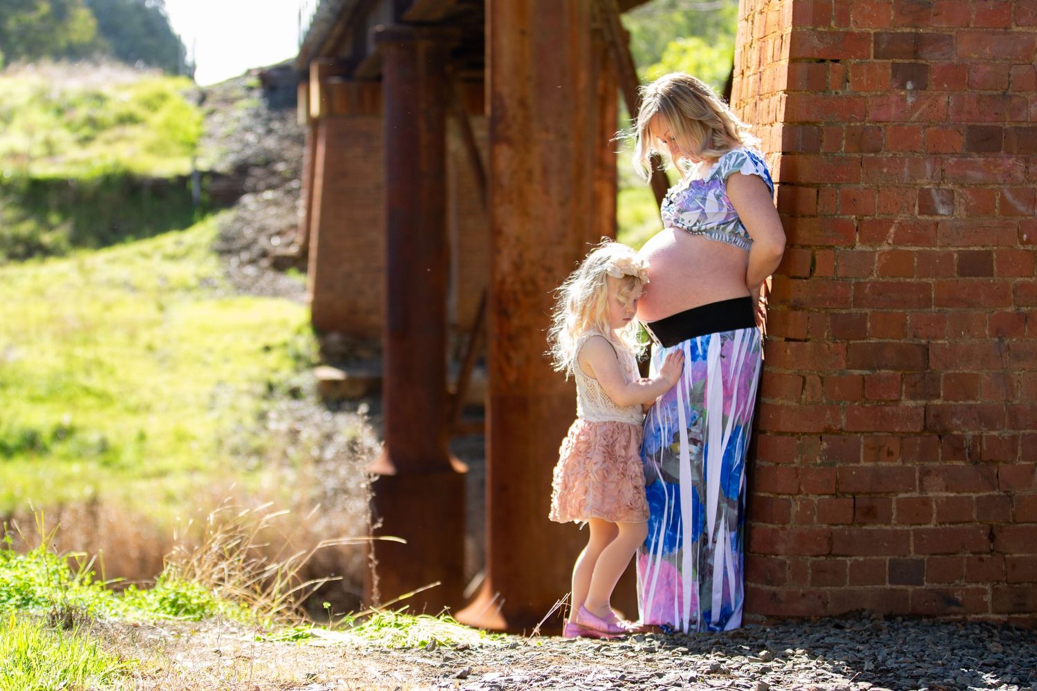 Parent and child share moment by rustic brick building in sunlight.