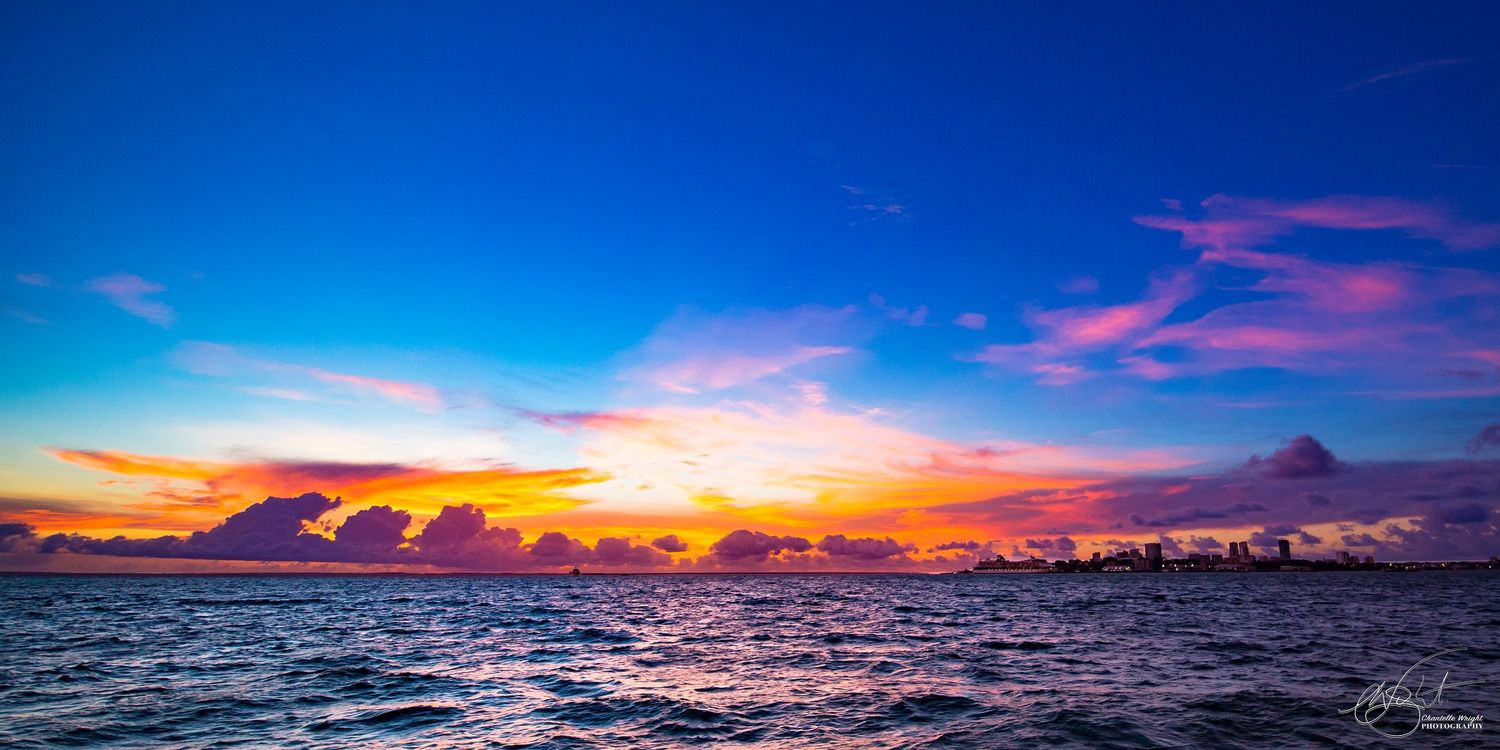 Vibrant sunset over ocean horizon with dramatic pink and orange clouds reflecting on dark blue waters.