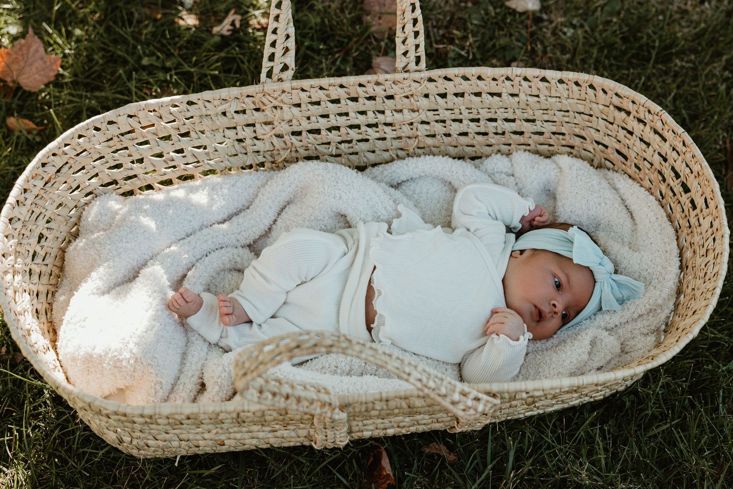 Newborn baby resting in woven moses basket with soft blue blanket.