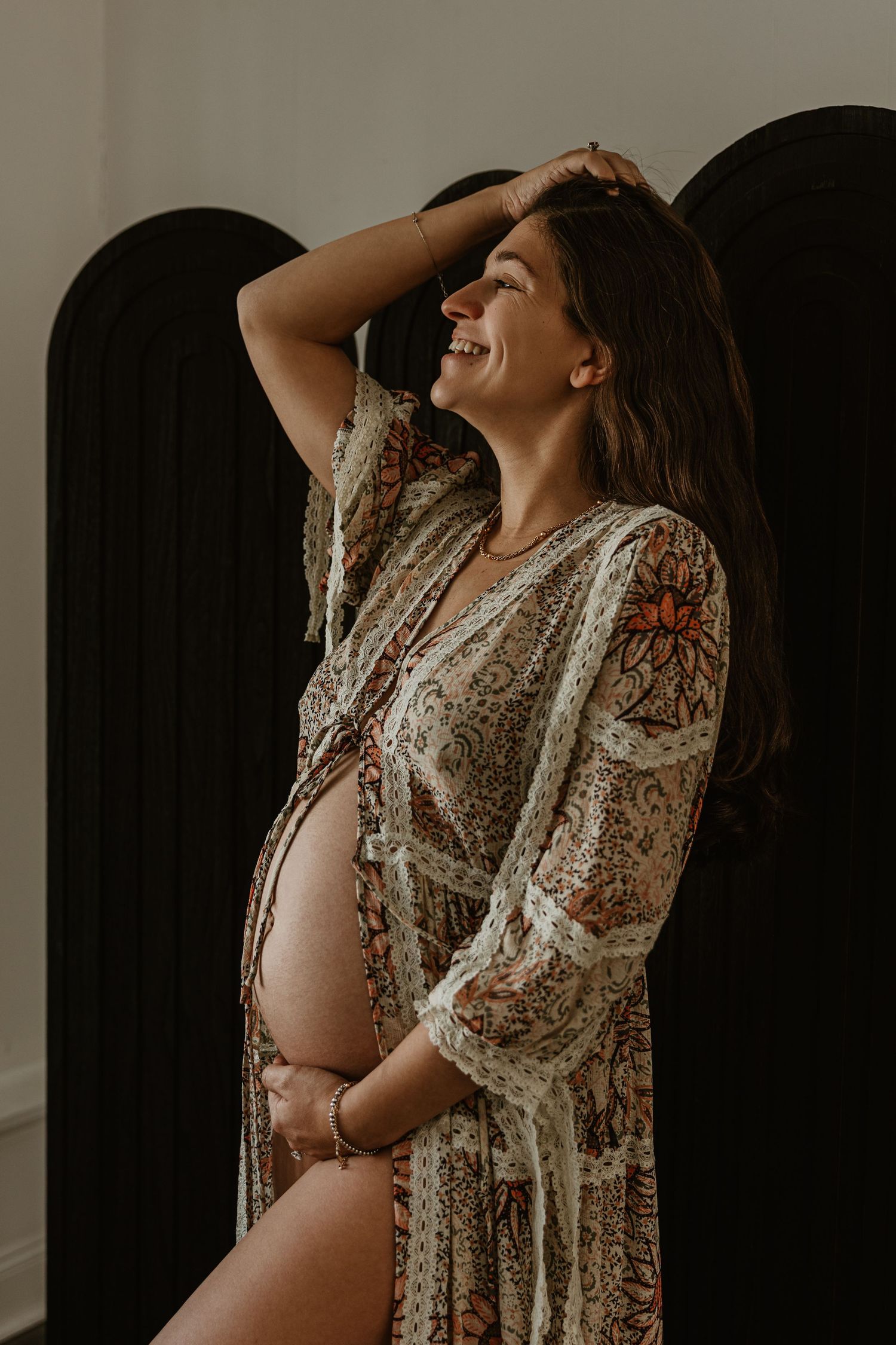 Dramatic maternity silhouette against dark background in lace robe.