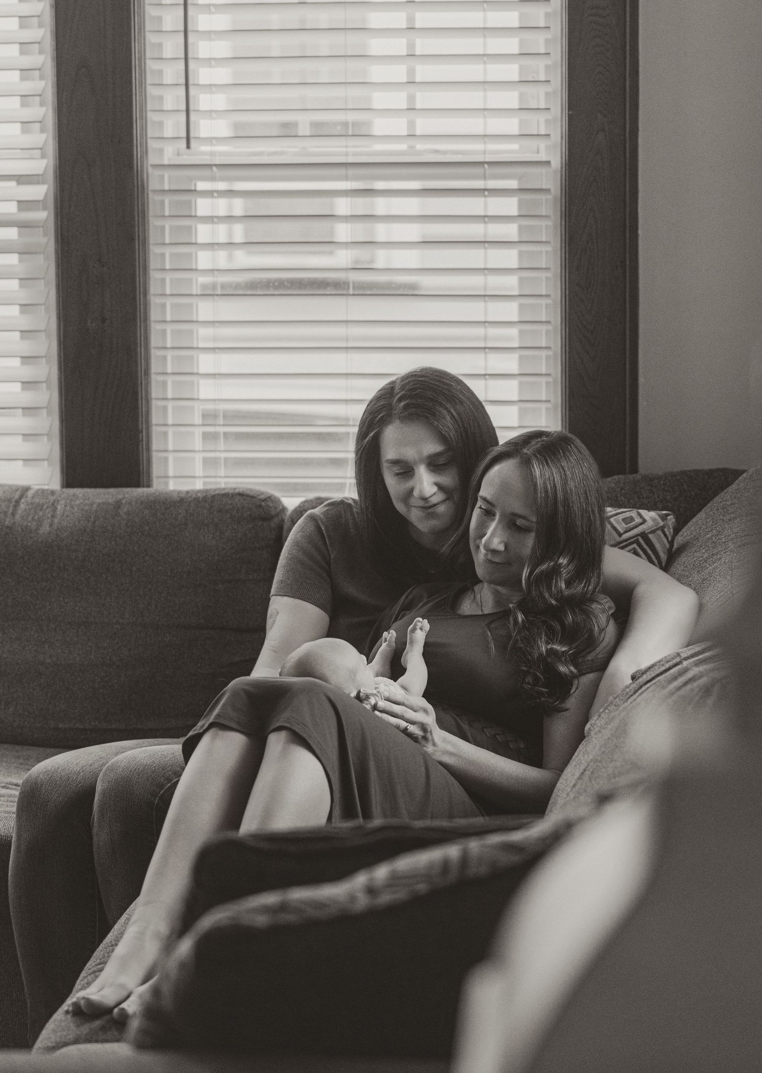 Two women sit closely together on a couch, sharing a phone in a cozy black and white indoor photo.