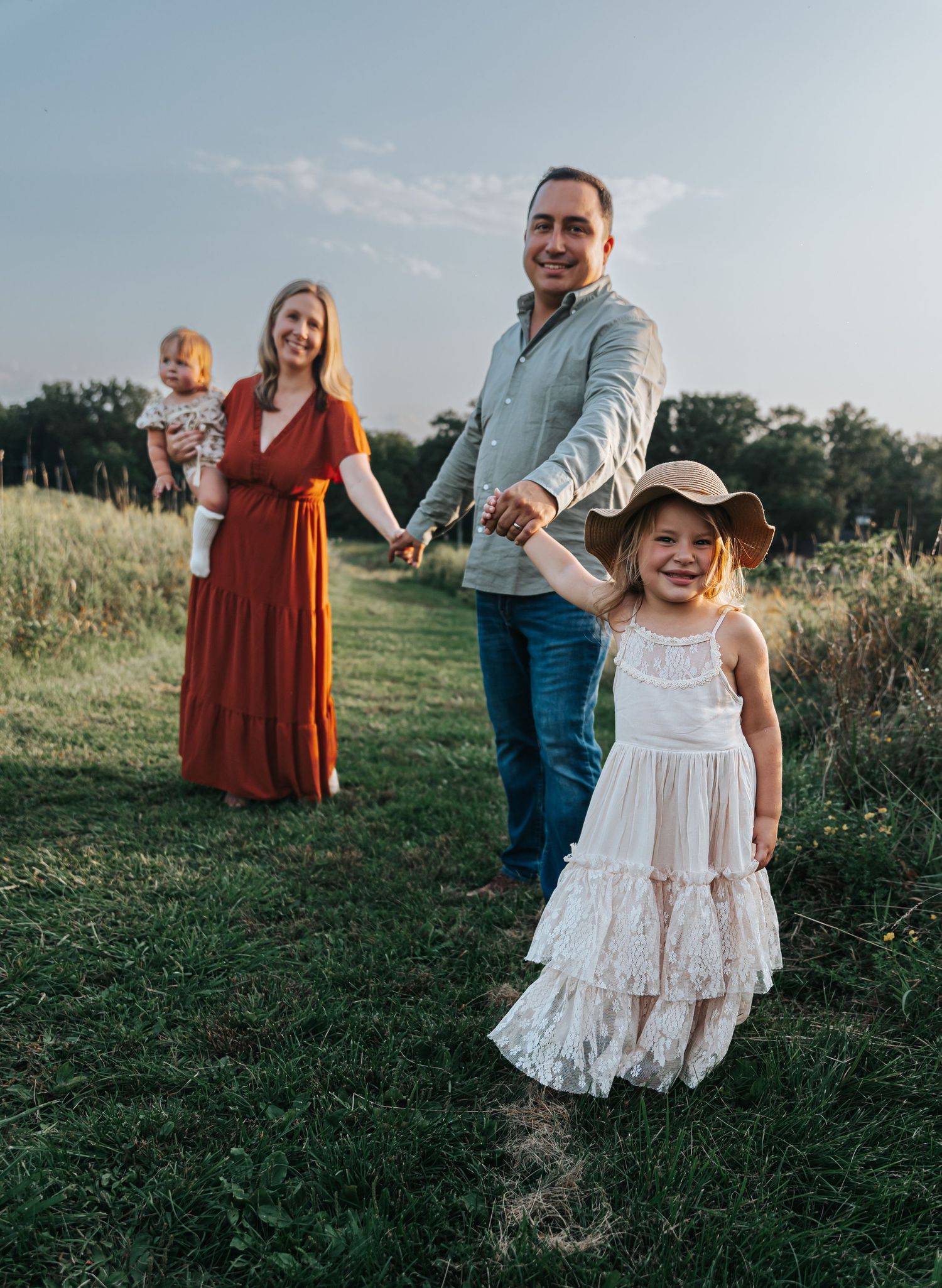 Candid outdoor family photoshoot in a summer field with white lace dress and rustic attire.