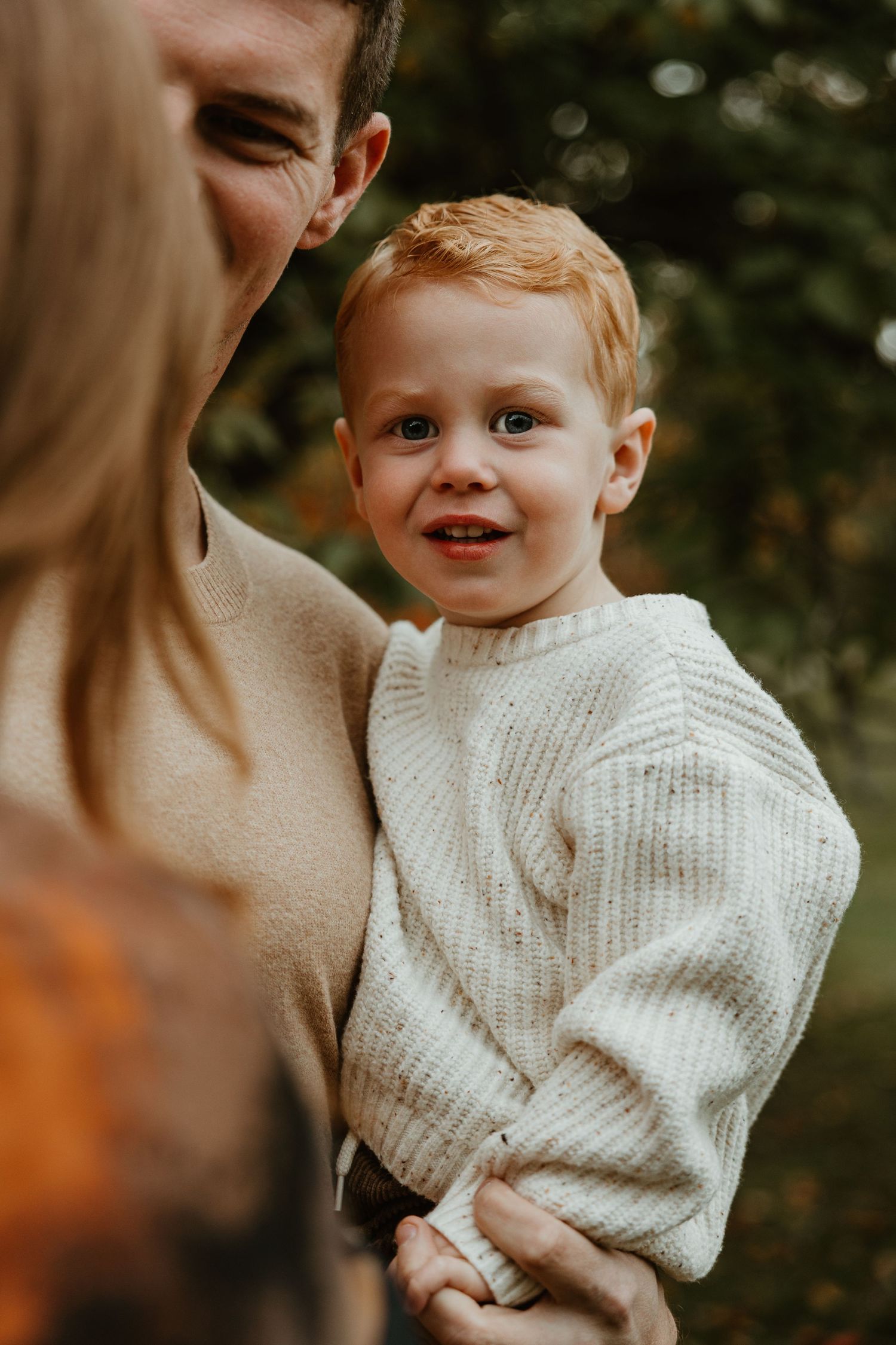 Close-up portrait of toddler in white knit sweater during autumn outdoor photoshoot.