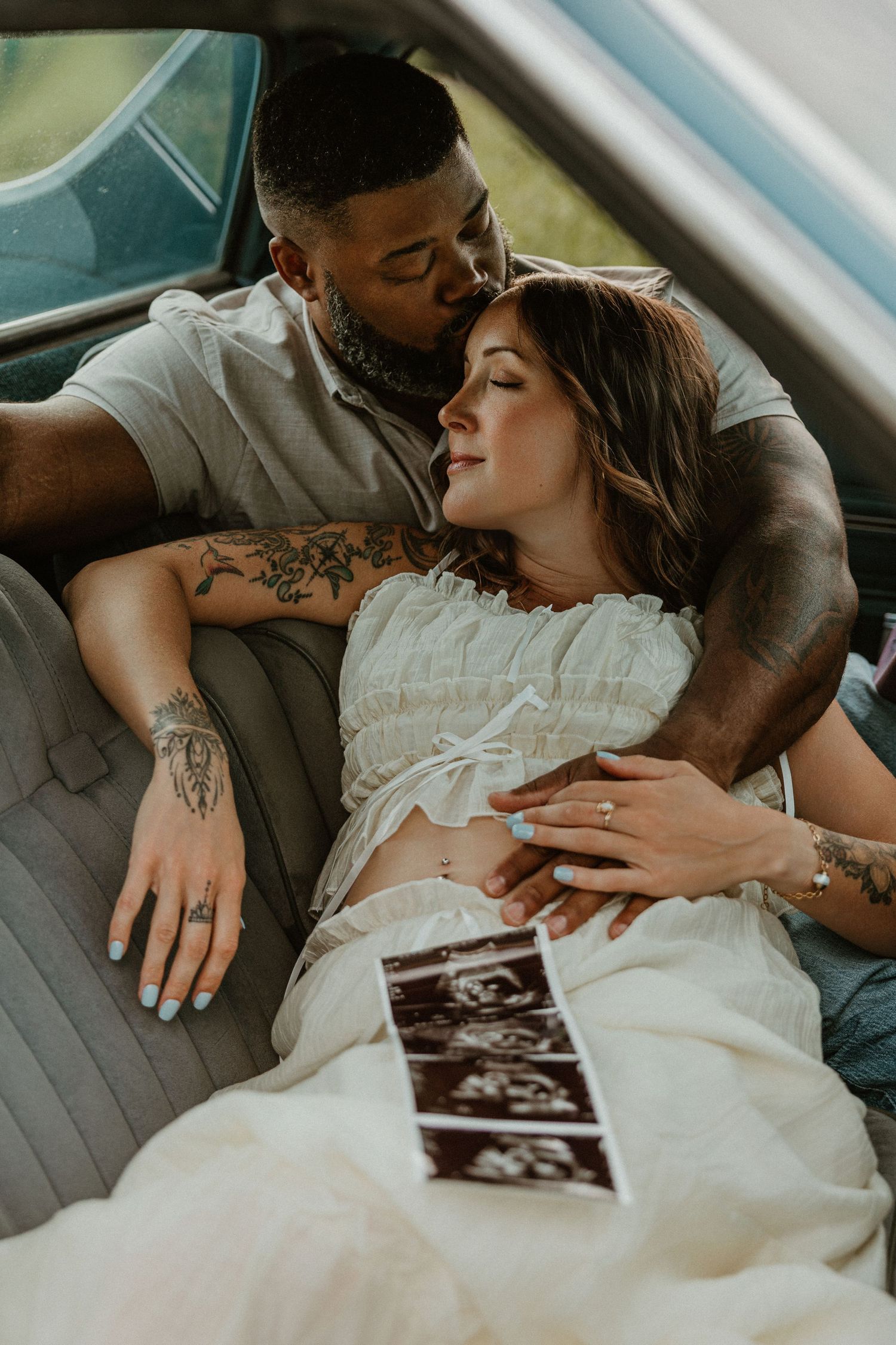 Couple sharing a tender moment in a vintage car, with ultrasound photos resting on her baby bump.