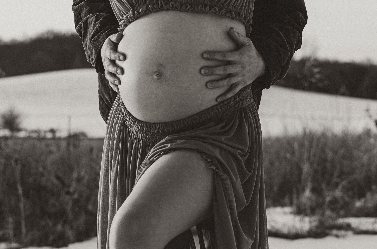 Black and white maternity portrait highlighting gentle embrace and flowing fabric.