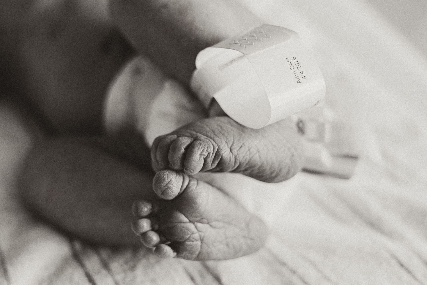 Close-up black and white photo of newborn baby feet with medical pulse oximeter tag attached.