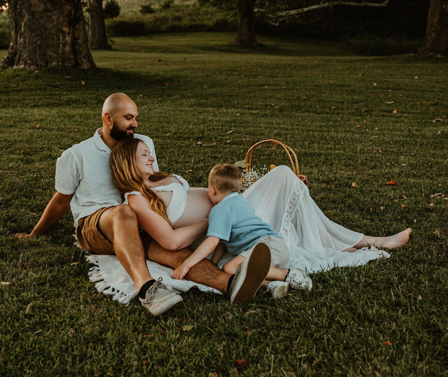 Family relaxing together on blanket in park during golden hour.