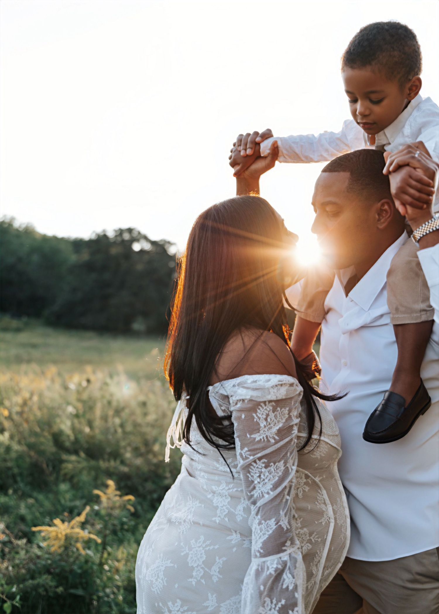 Family maternity photoshoot in a golden field at sunset wearing coordinated white outfits.