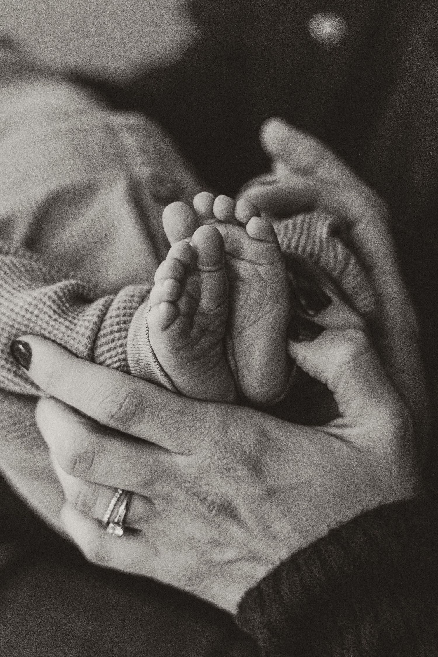 Close-up black and white image of hands holding each other with a ring visible.