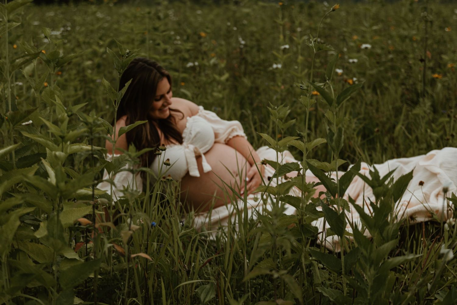 Expectant mother relaxes on blanket in field of wildflowers.