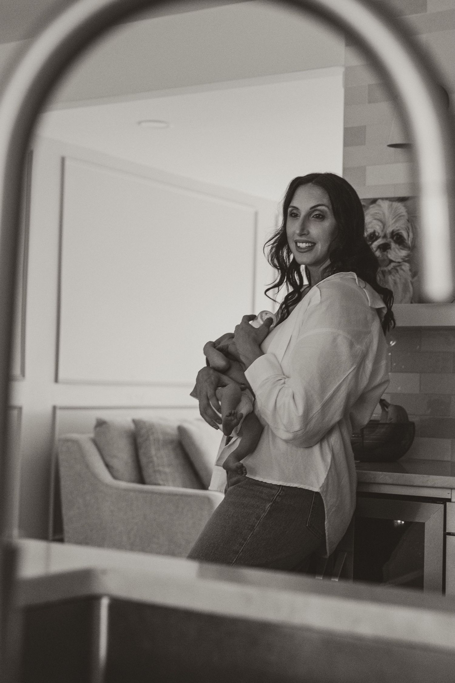 Black and white photo of a woman smiling in a kitchen holding something close to her chest.