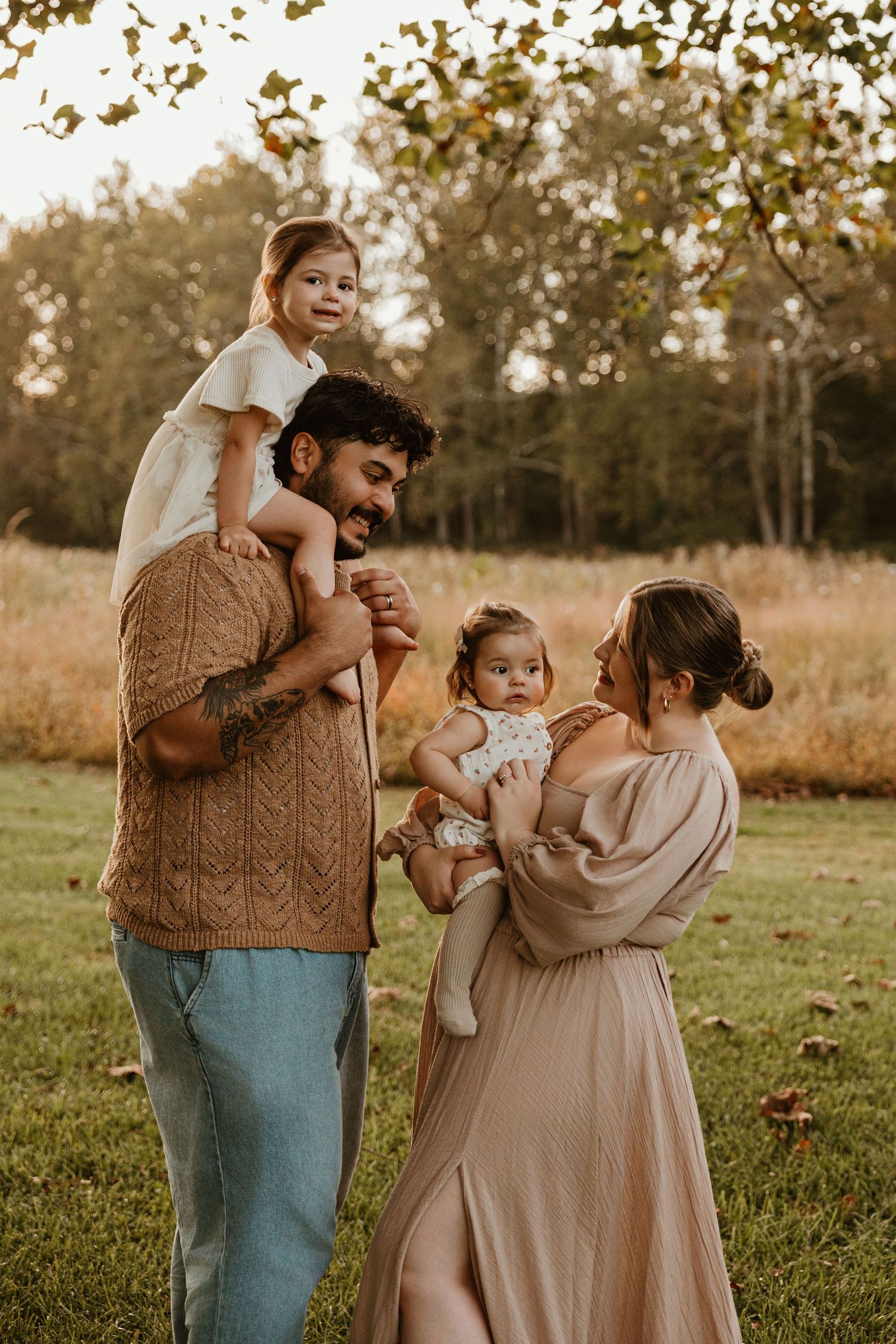 Family shares playful interactions during sunset photoshoot in field.