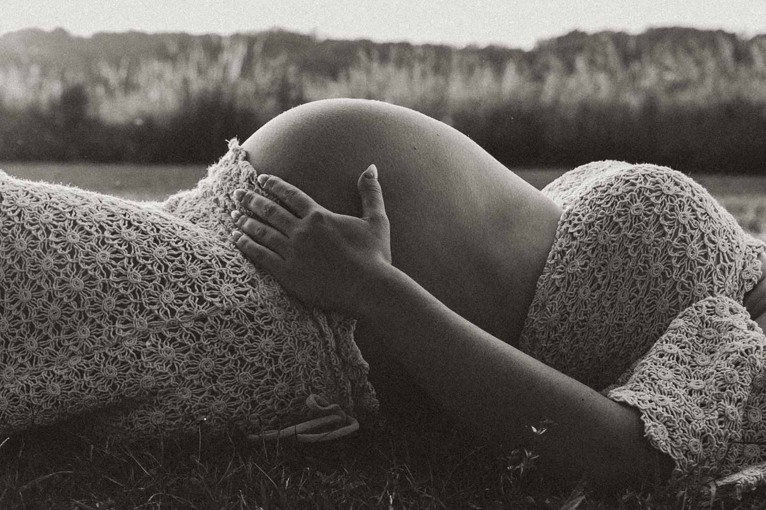 Black and white artistic maternity photograph showing gentle hands cradling a pregnant belly.