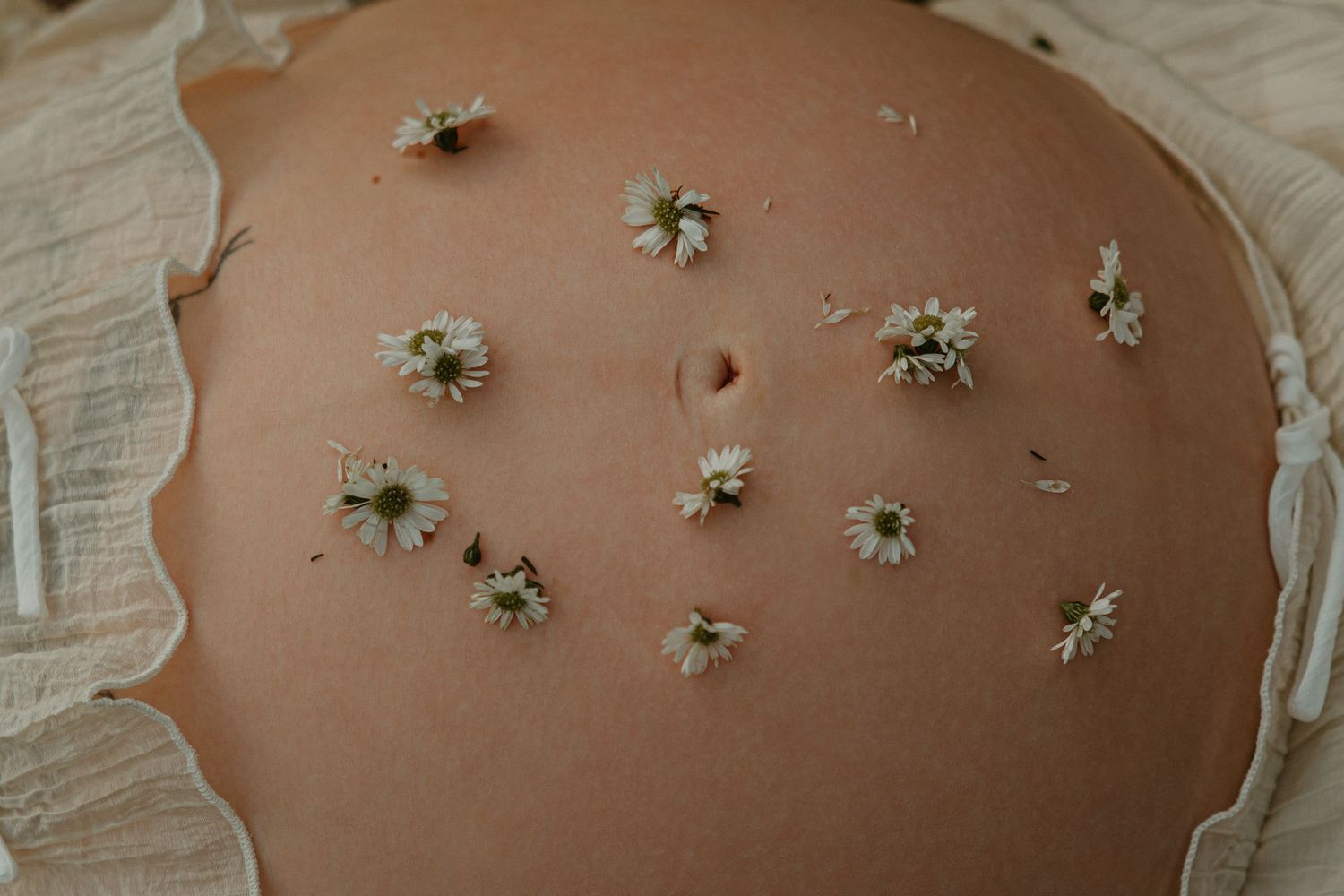Pregnant belly adorned with delicate white daisy flowers arranged artistically on bare skin during maternity photoshoot.