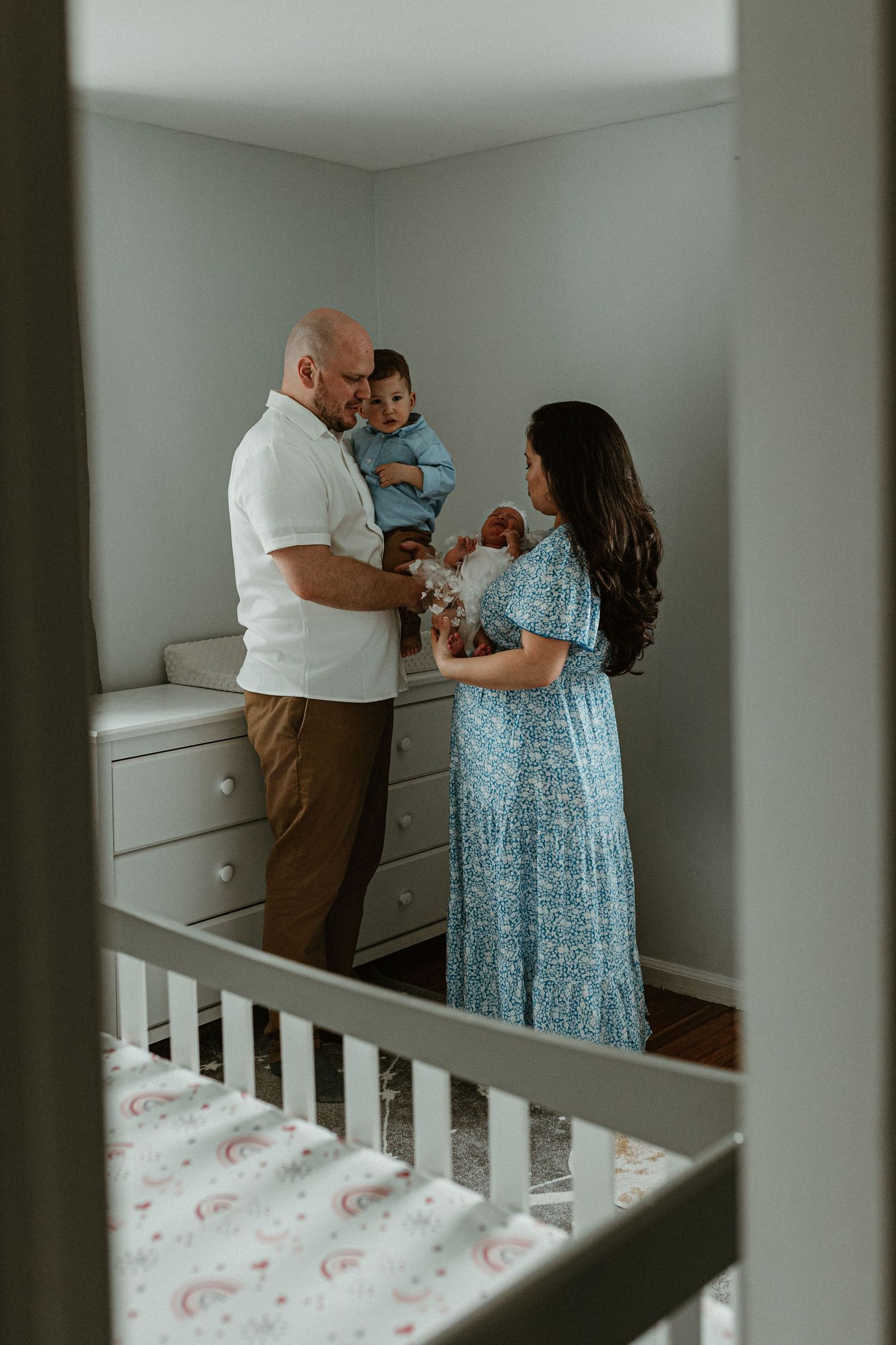 A nursery scene with a white crib and family members interacting near a changing table.