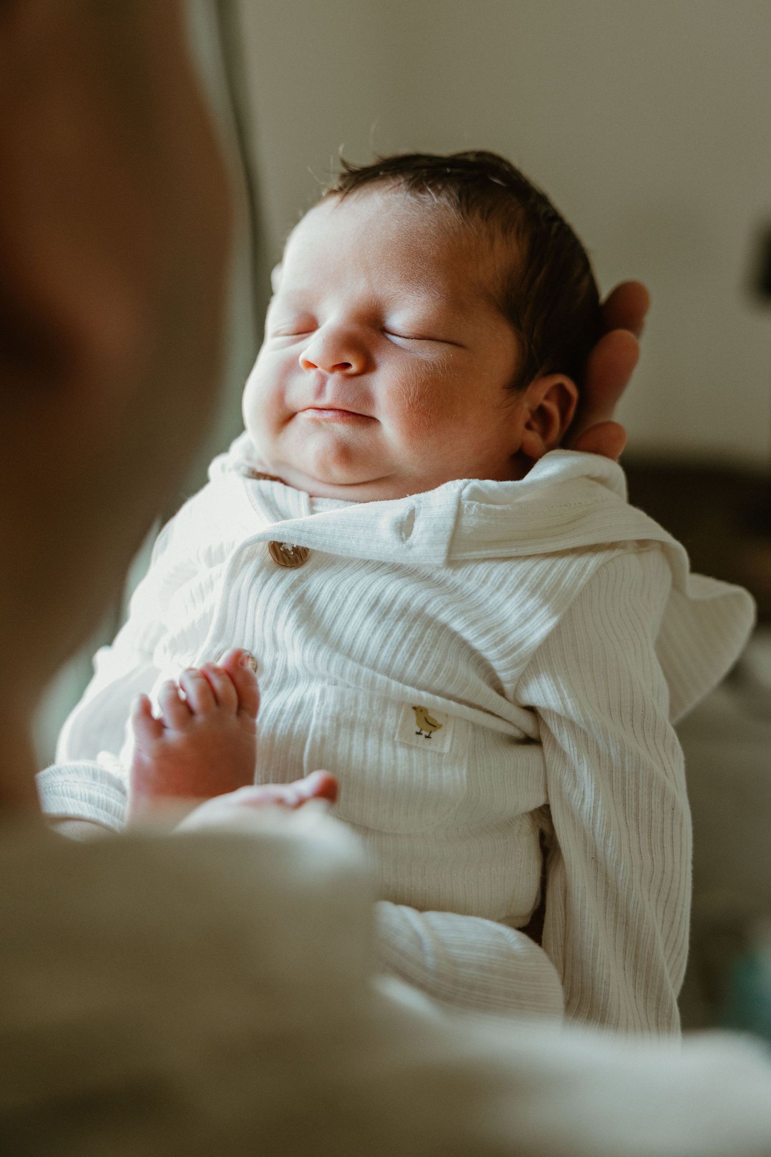 Peaceful newborn baby sleeping contentedly in white outfit while being held by parent.