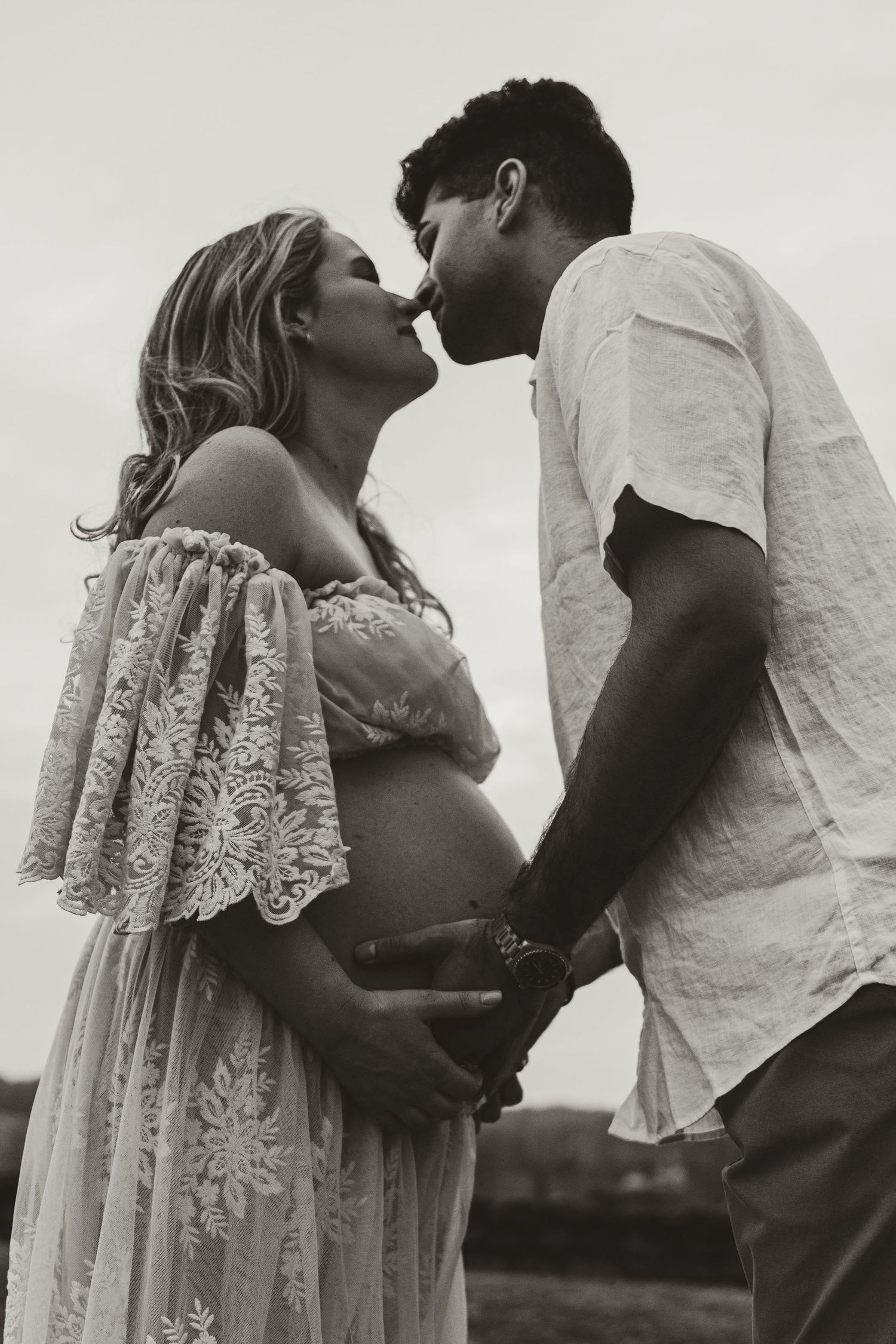 Intimate black and white photo of expecting couple sharing tender moment in lace dress and white shirt.